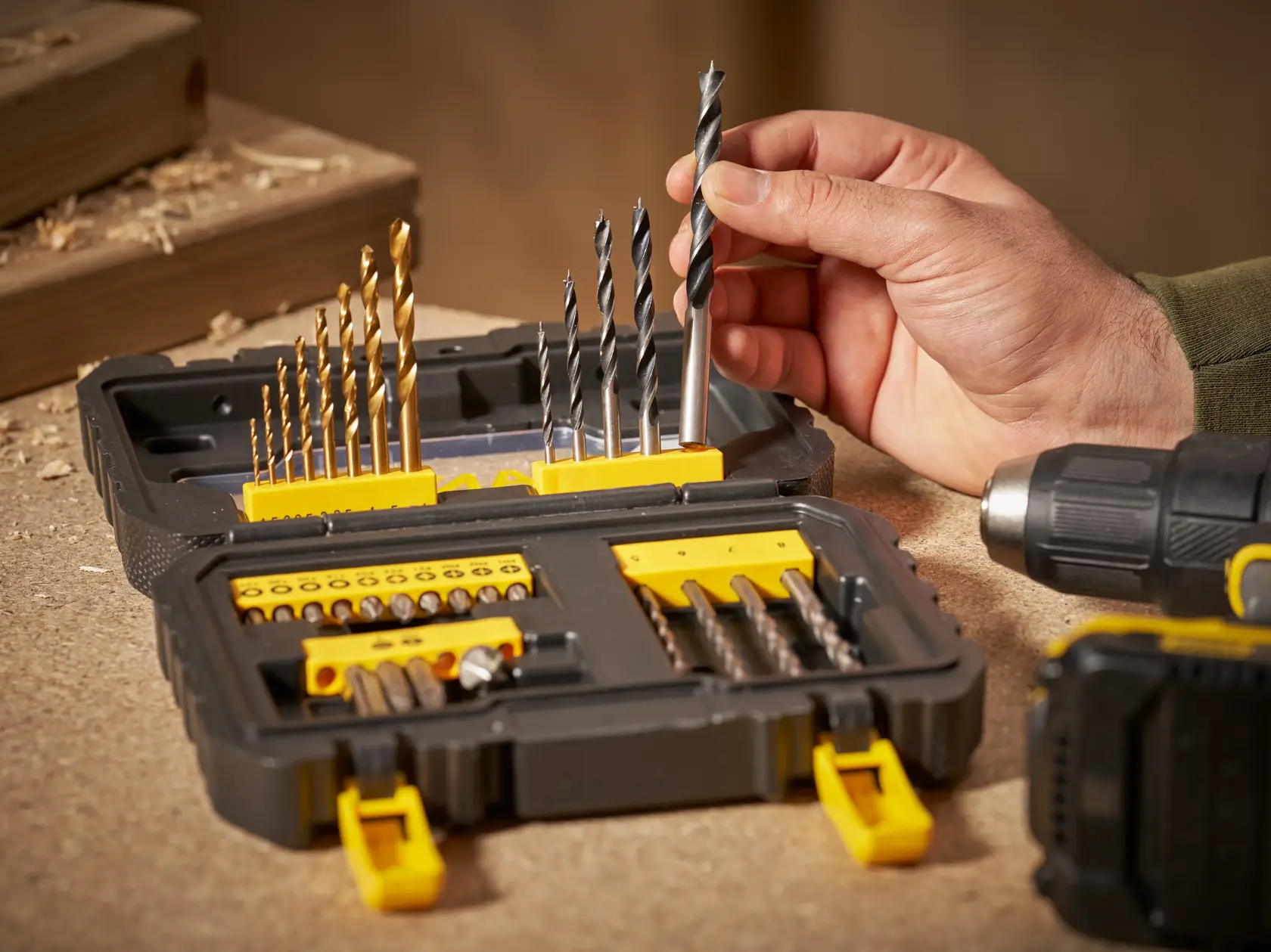 STANLEY STA88550 drill bit and accessory set open on workbench, hand selecting a drill bit, side angle.