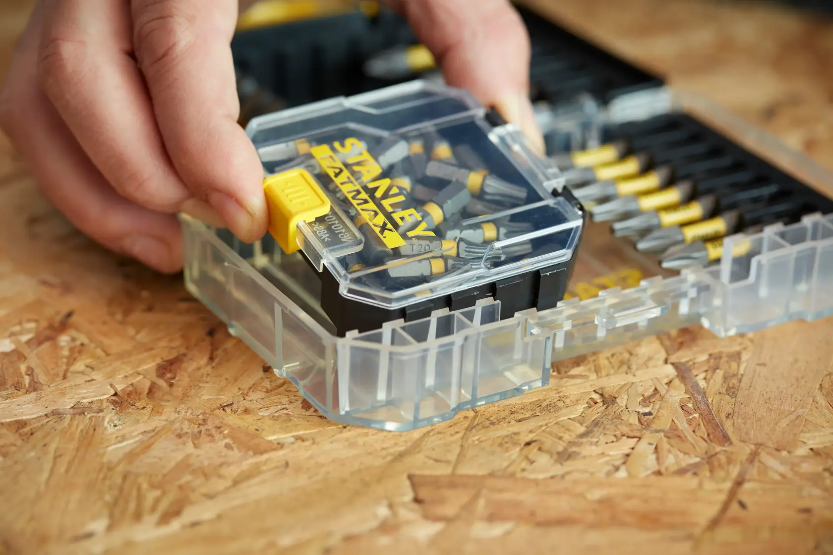 STANLEY STA88566 Schrauber-Bit-Set mit Klarsichtbox, Nahaufnahme einer Hand am gelben Verschluss.