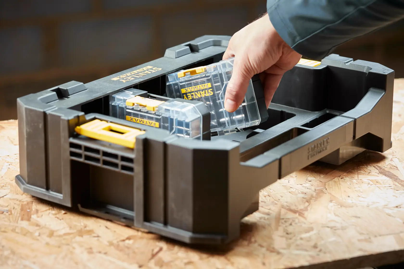 STANLEY STA88580 Organizer-Ablage mit herausnehmbaren durchsichtigen Kunststoffboxen auf Werkbank, Hand nimmt eine Box.