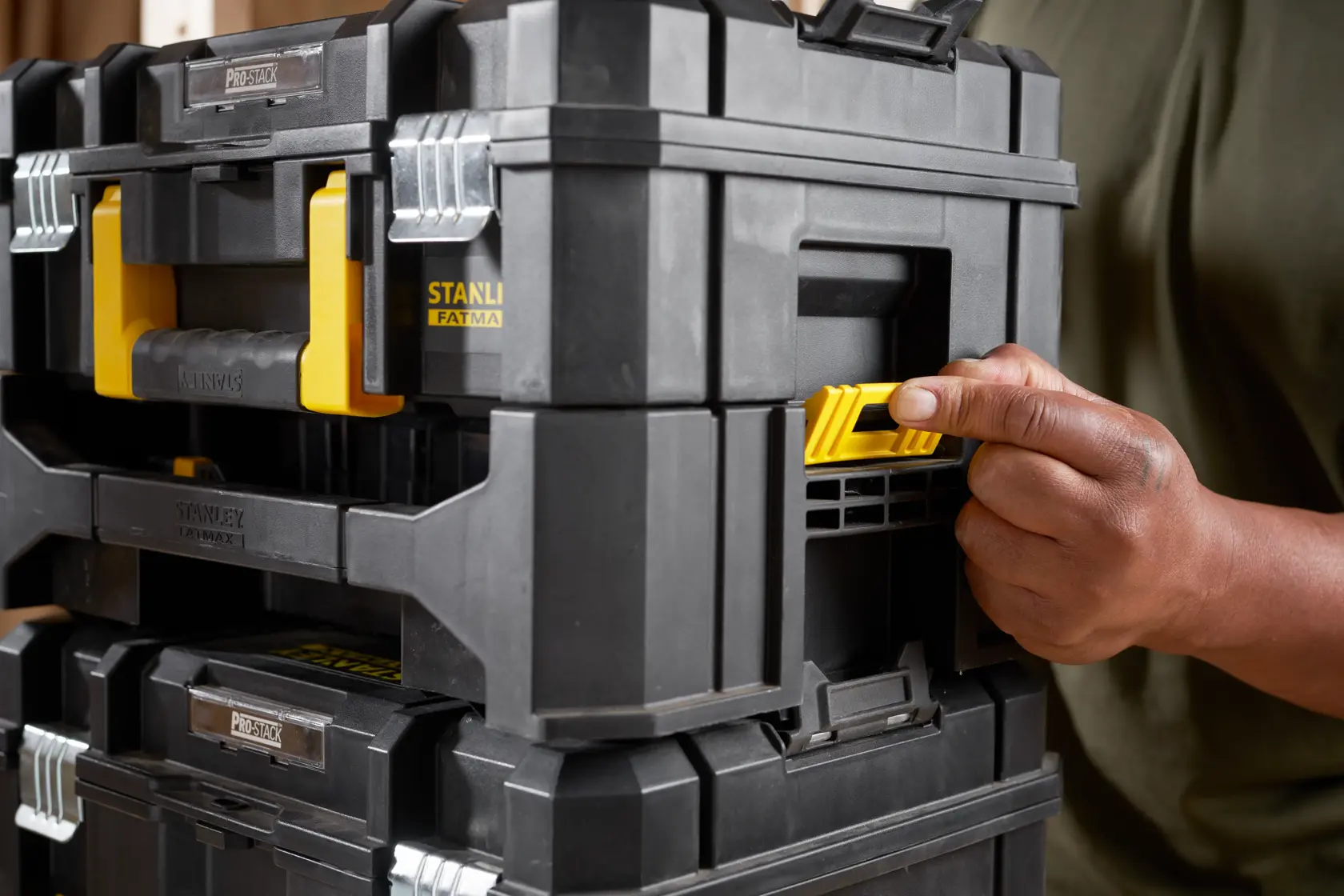 STANLEY STA88580 PROSTACK Werkzeugbox in Schwarz und Gelb, Nahaufnahme seitlich, Hand drückt gelben Riegel.