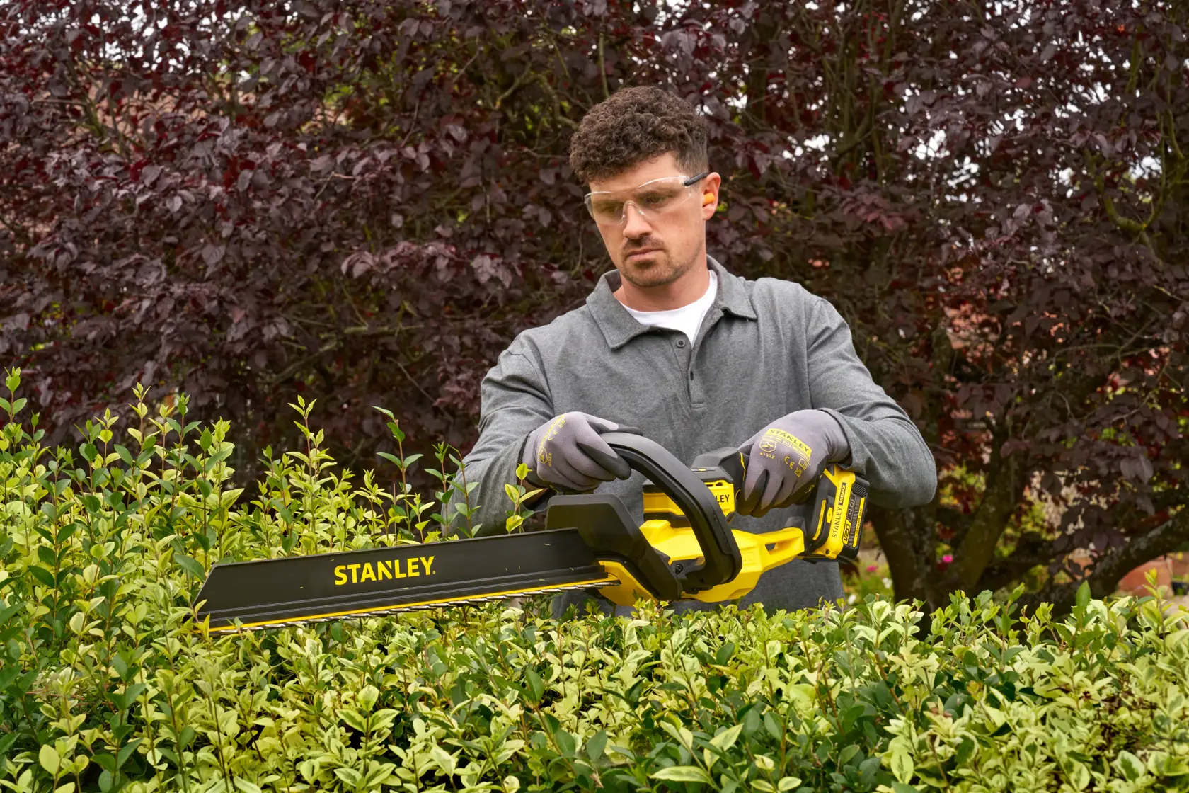 Foto einer Person, die im Garten einen STANLEY STCHT8255B Heckenschneider zum Schneiden grüner Büsche verwendet.