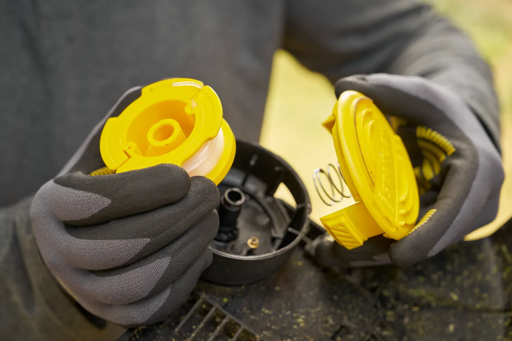 STANLEY STCST933B Trimmer-Spulenmontage Fotografie, Nahaufnahme gelbe Spule und Abdeckung in behandschuhten Händen.