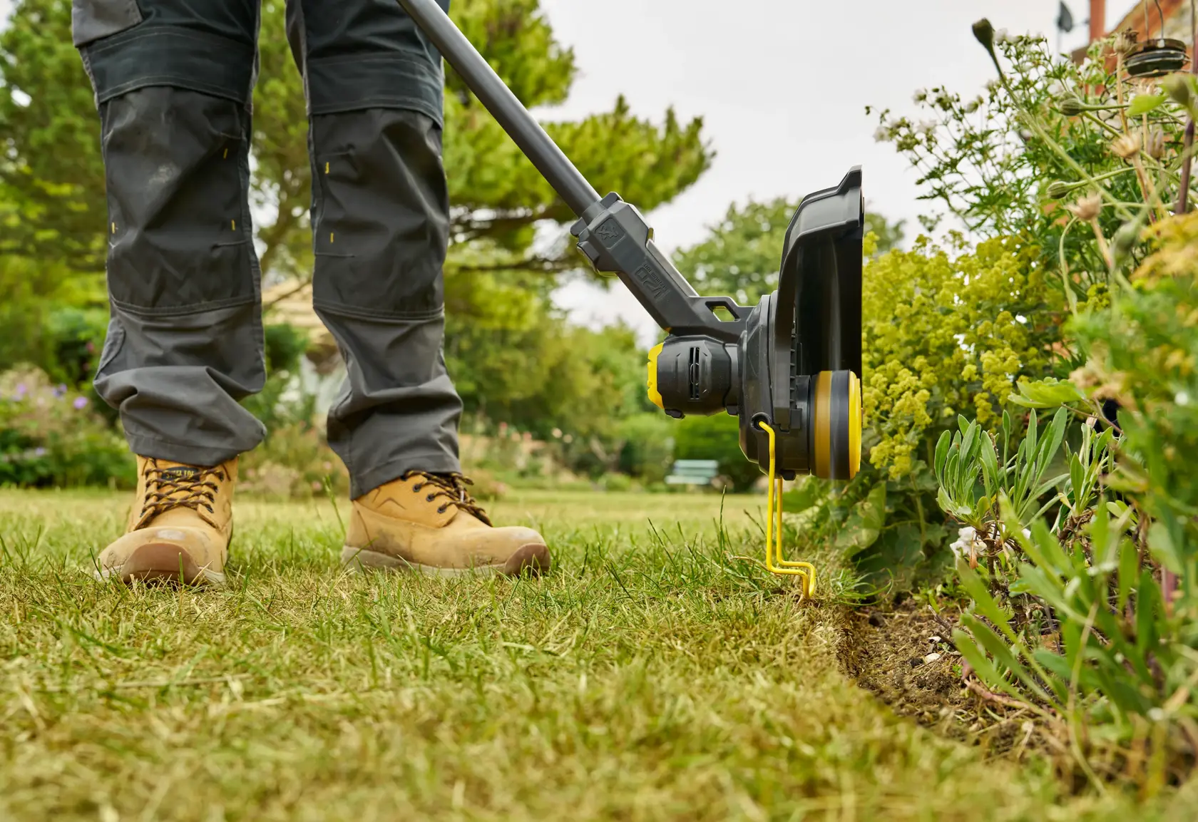 STANLEY STCST933M1 Rasentrimmer in Benutzung, Seitenansicht, trimmt Rasenkante neben Gartenpflanzen.