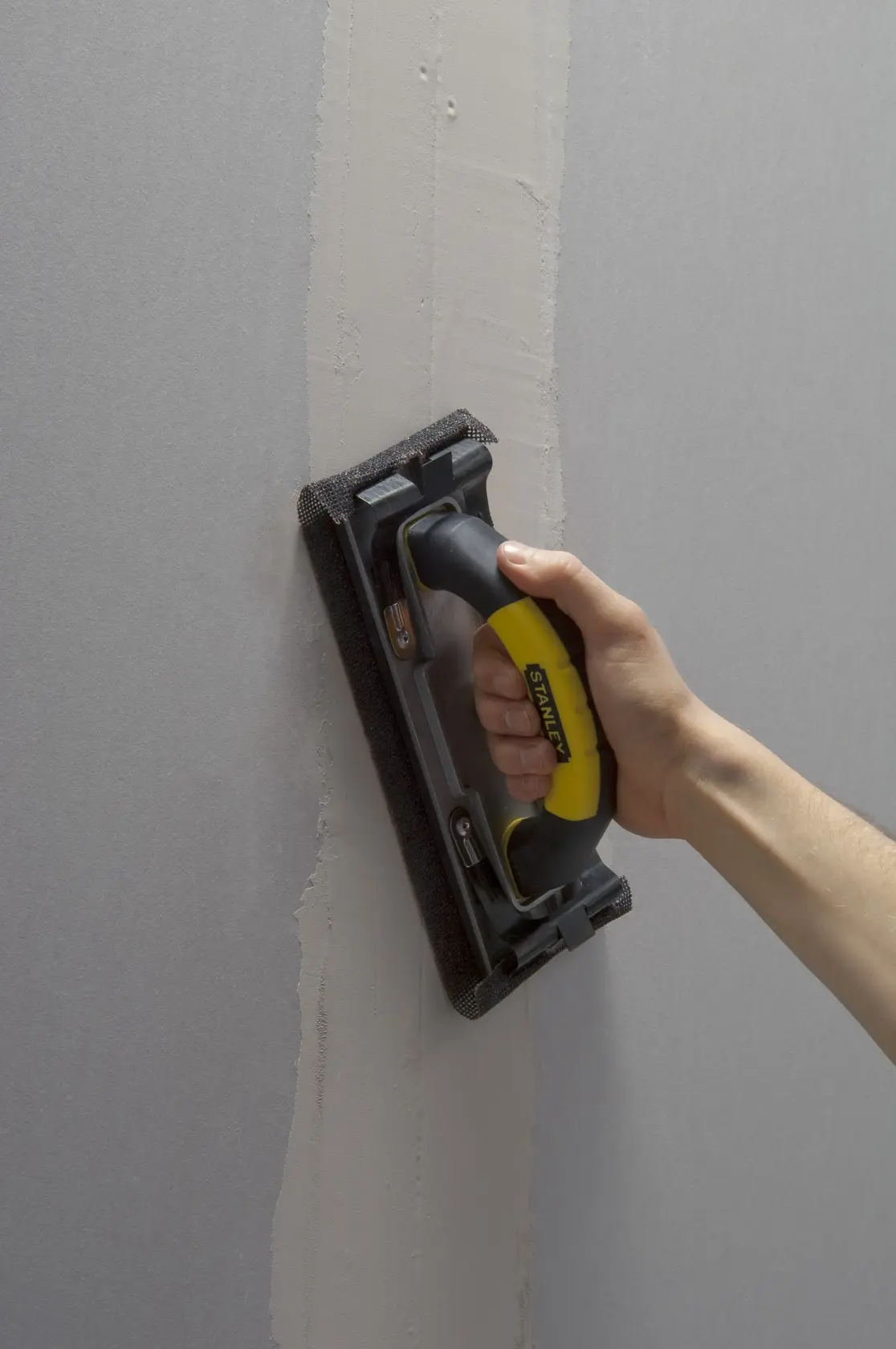 Foto des STANLEY STHT0-05927 Handschleifers mit schwarz-gelbem Griff auf Wandoberfläche.