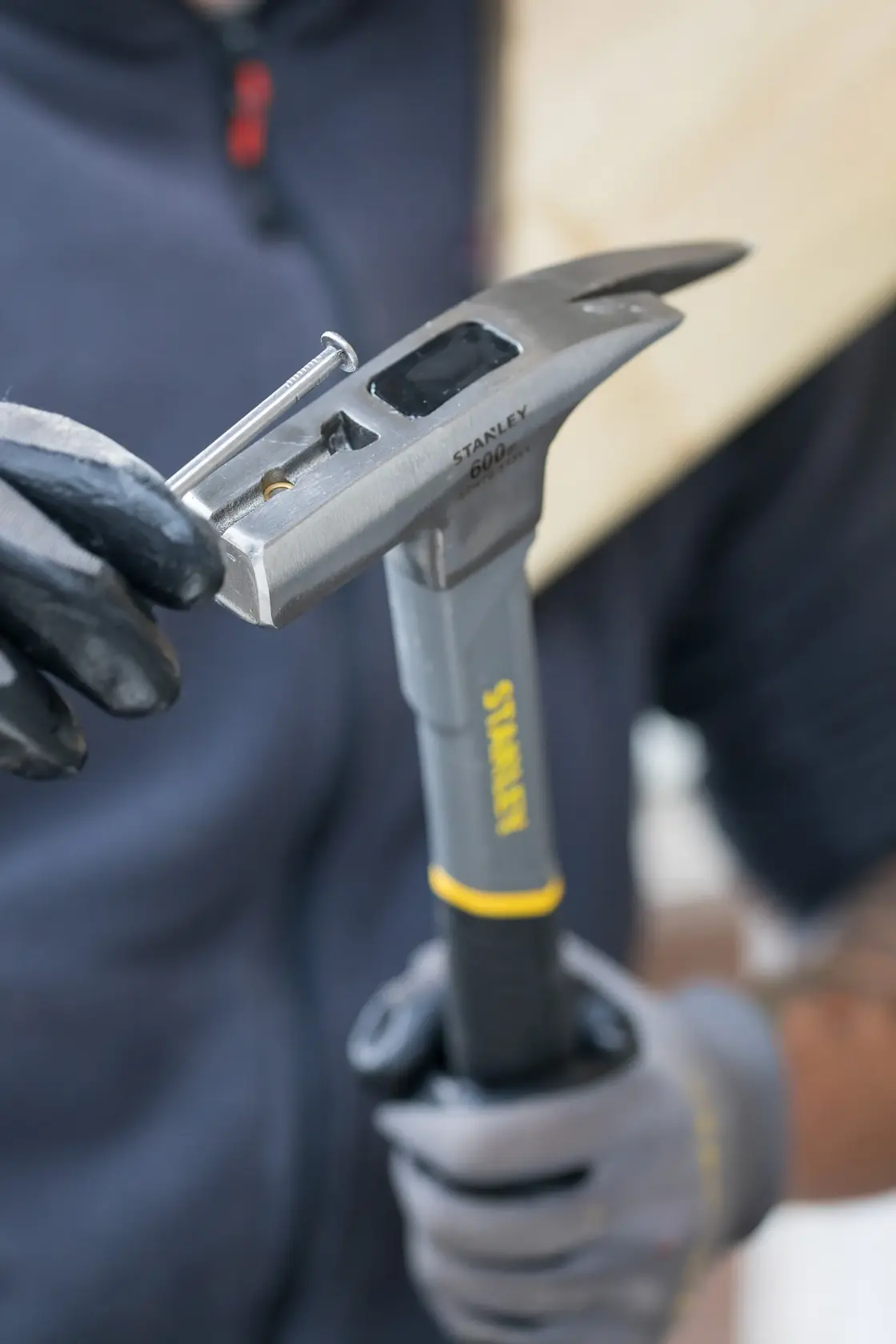 STANLEY STHT0-51311 hammer held in gloved hands, showing nail starter feature in use.