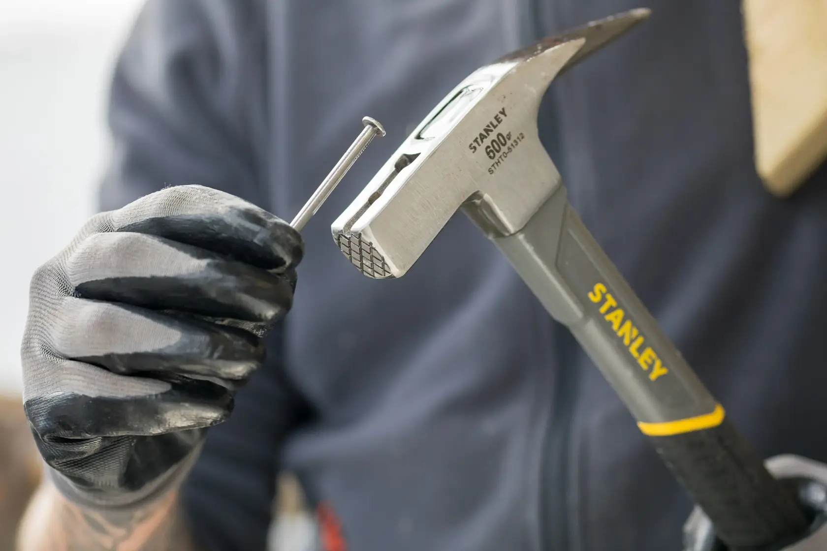 Stanley STHT0-51312 Hammer mit Handschuh gehalten, Nagel positioniert, Nahaufnahme.