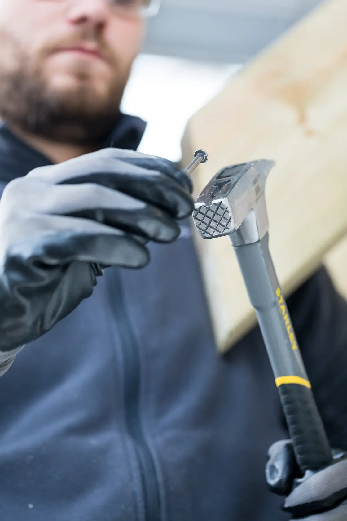 Foto des STANLEY STHT0-51312 Stahlklauenhammers in behandschuhter Hand, positioniert einen Nagel auf einem Holzbrett.