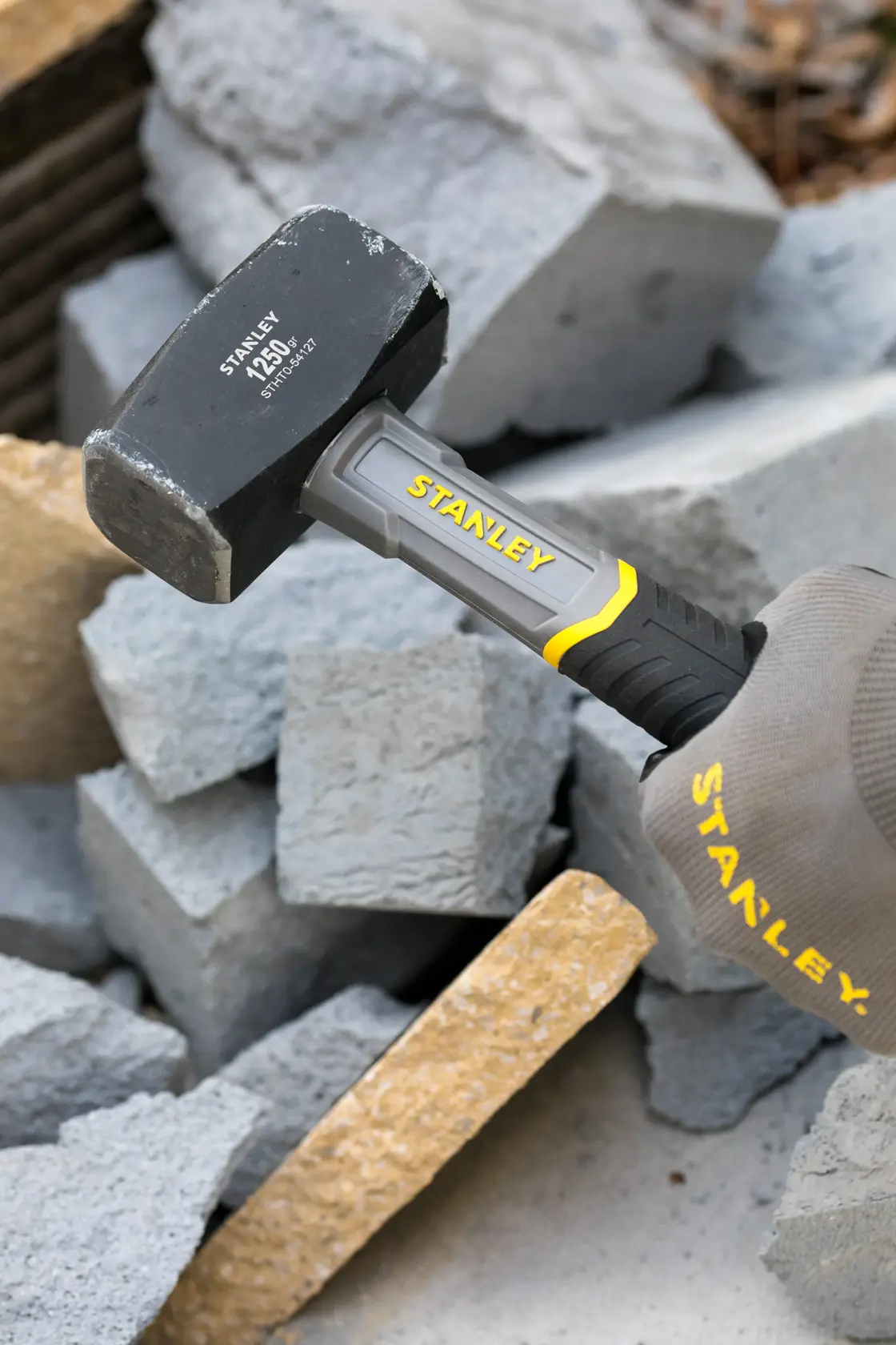 Foto des STANLEY STHT0-54127 Vorschlaghammers mit grauem und gelbem Griff beim Zerschlagen von Betonblöcken.