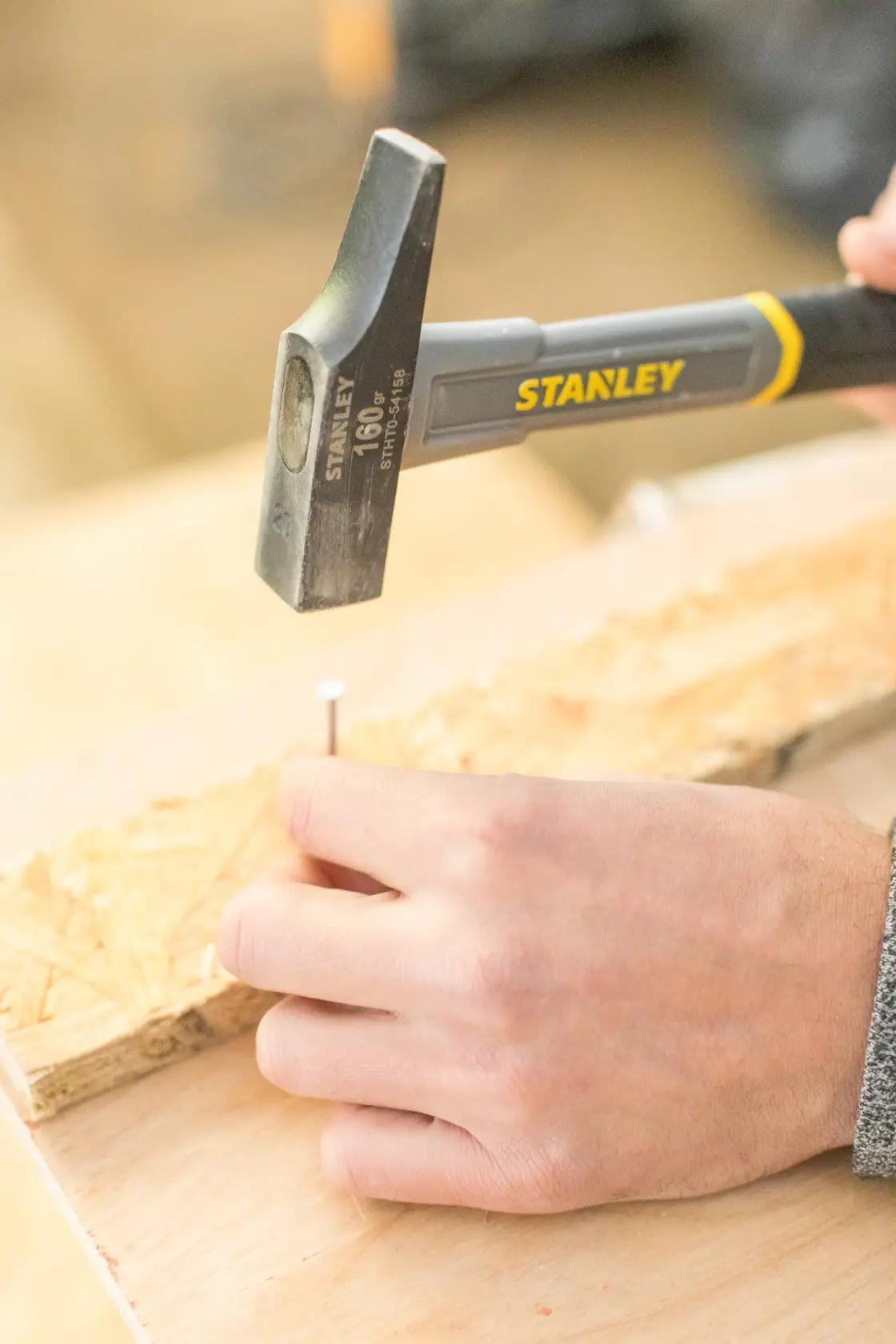 STANLEY STHT0-54158 Klauenhammer beim Einschlagen eines Nagels ins Holz, Nahaufnahme Fotografie.