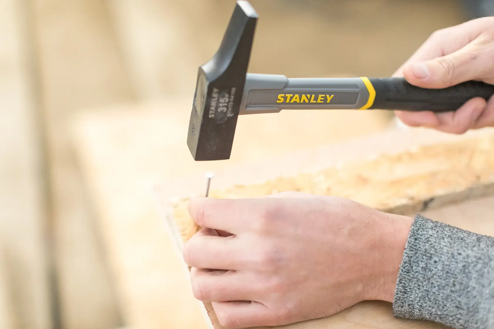 STANLEY STHT0-54159 Hammer treibt Nagel ins Holz, Nahaufnahme von Händen und Werkzeug.