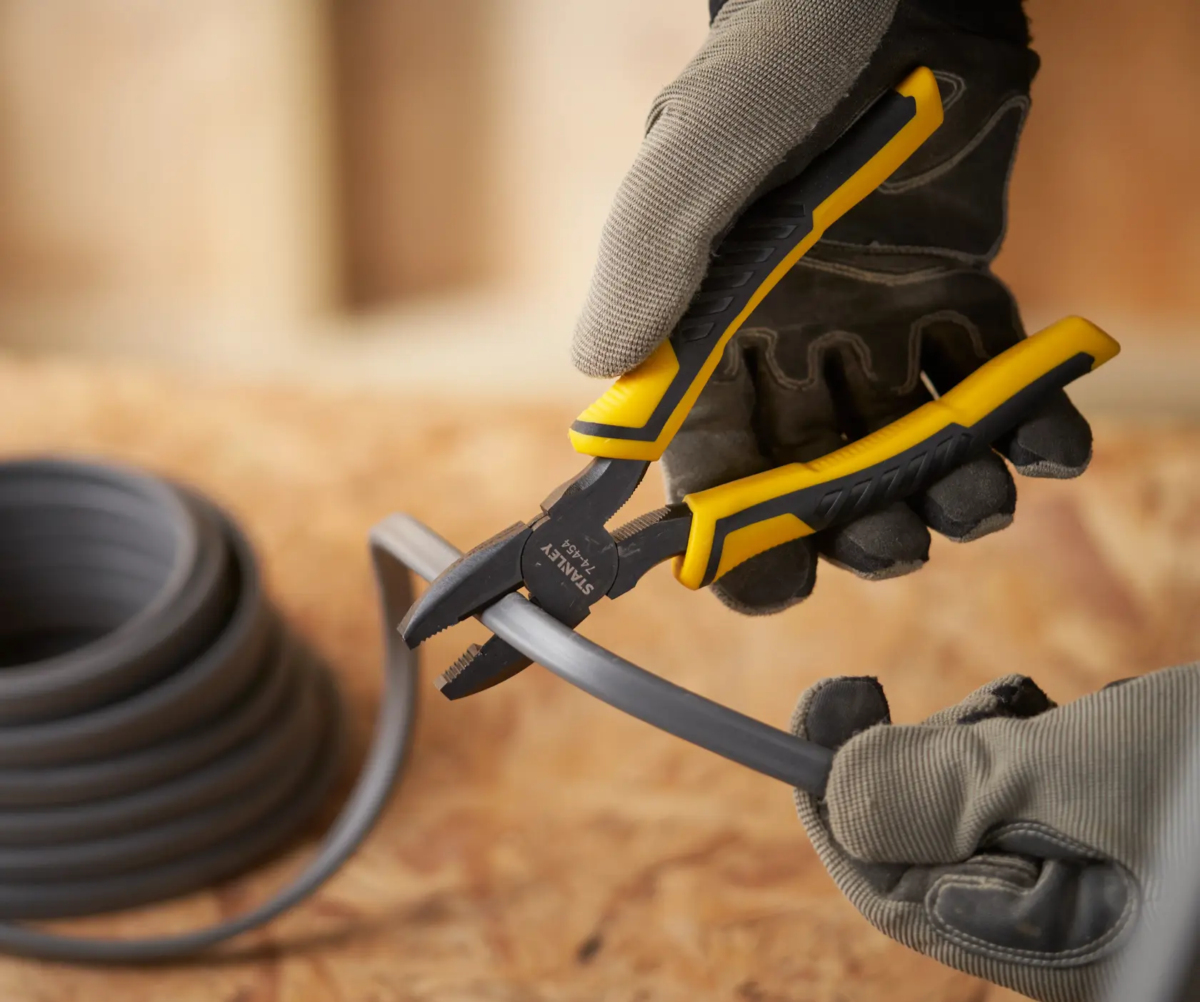 Photo of STANLEY STHT0-74367 pliers cutting plastic tubing, worker wearing gloves.