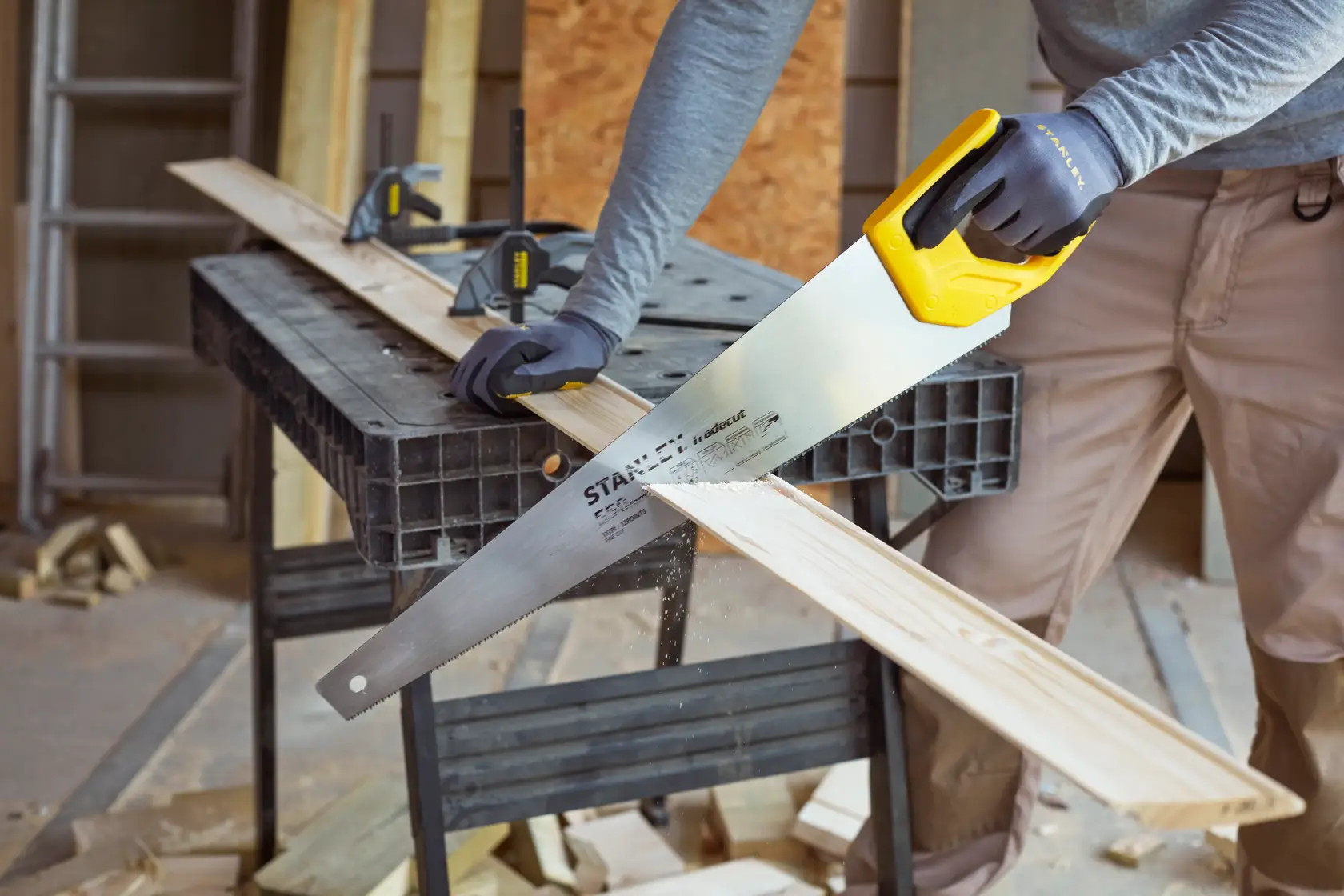 STANLEY STHT1-20353 Handsäge mit gelbem Griff schneidet Holzbrett in Werkstattumgebung.