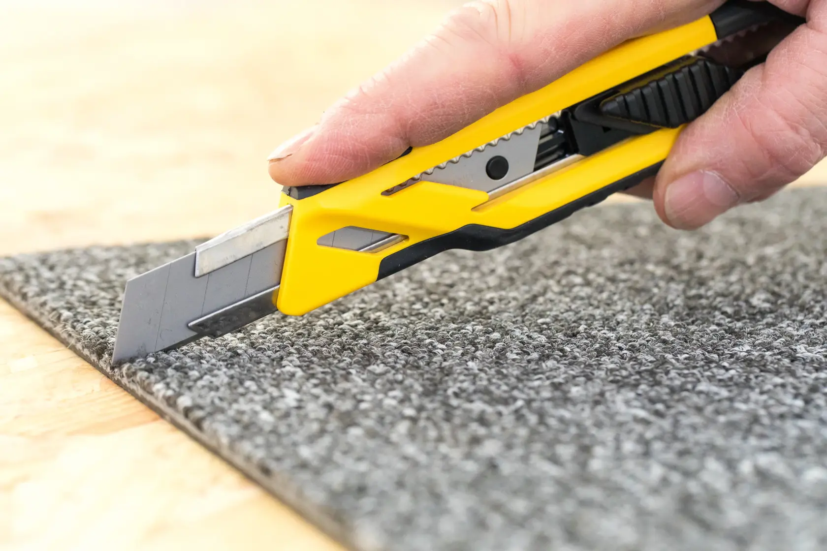 STANLEY STHT10266-1 Universalmesser schneidet grauen Teppich, Seitenansicht, gelb-schwarzer Griff.