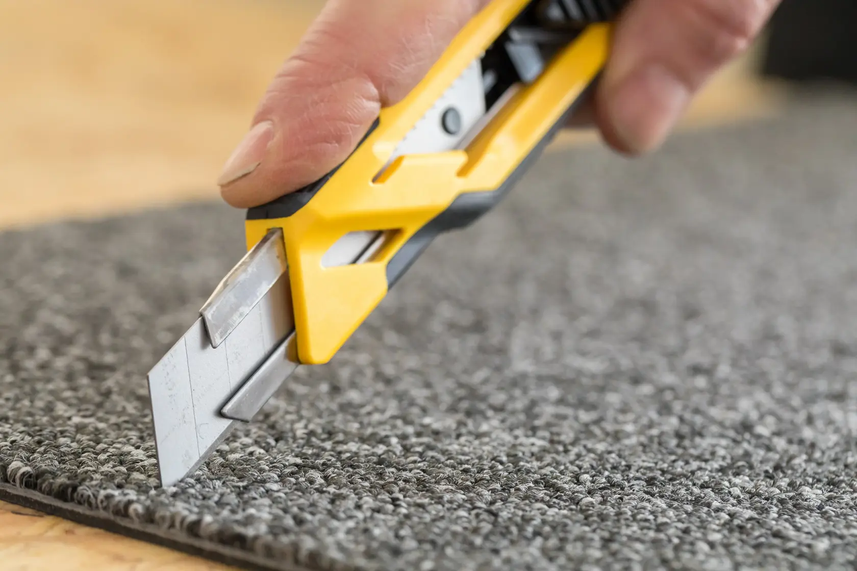 Nahaufnahme einer Hand, die mit einem gelben Messer einen grauen Teppich schneidet.