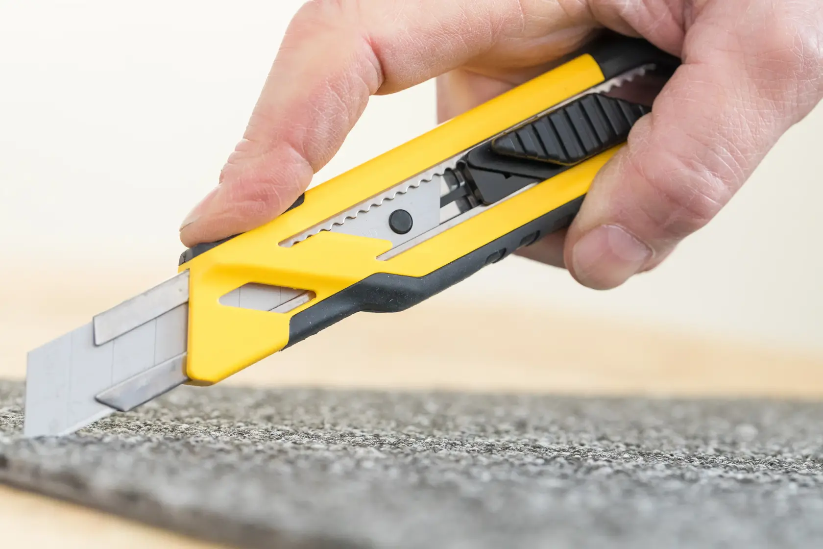 STANLEY STHT10266-1 Universalmesser mit gelb-schwarzem Gehäuse schneidet Teppich, Nahaufnahme Fotografie.