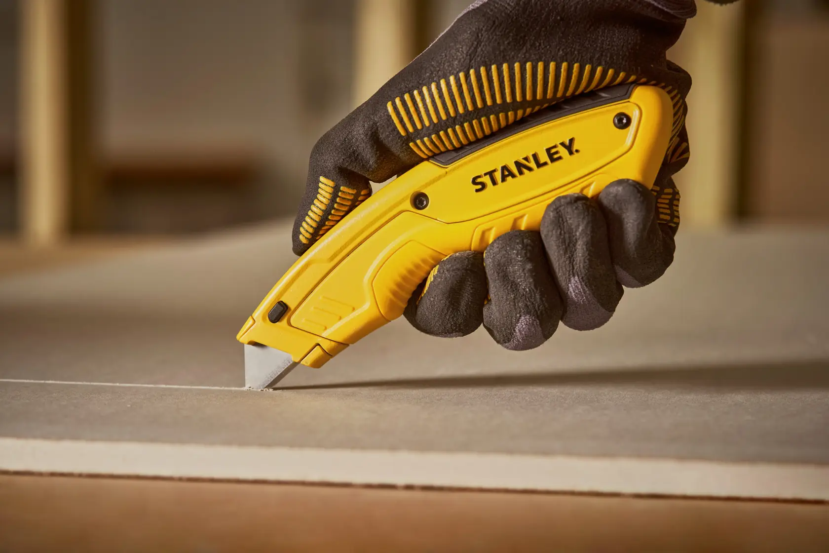 Foto des STANLEY STHT10430-0 Universalmessers, das Trockenbau schneidet, gehalten von einer behandschuhten Hand.