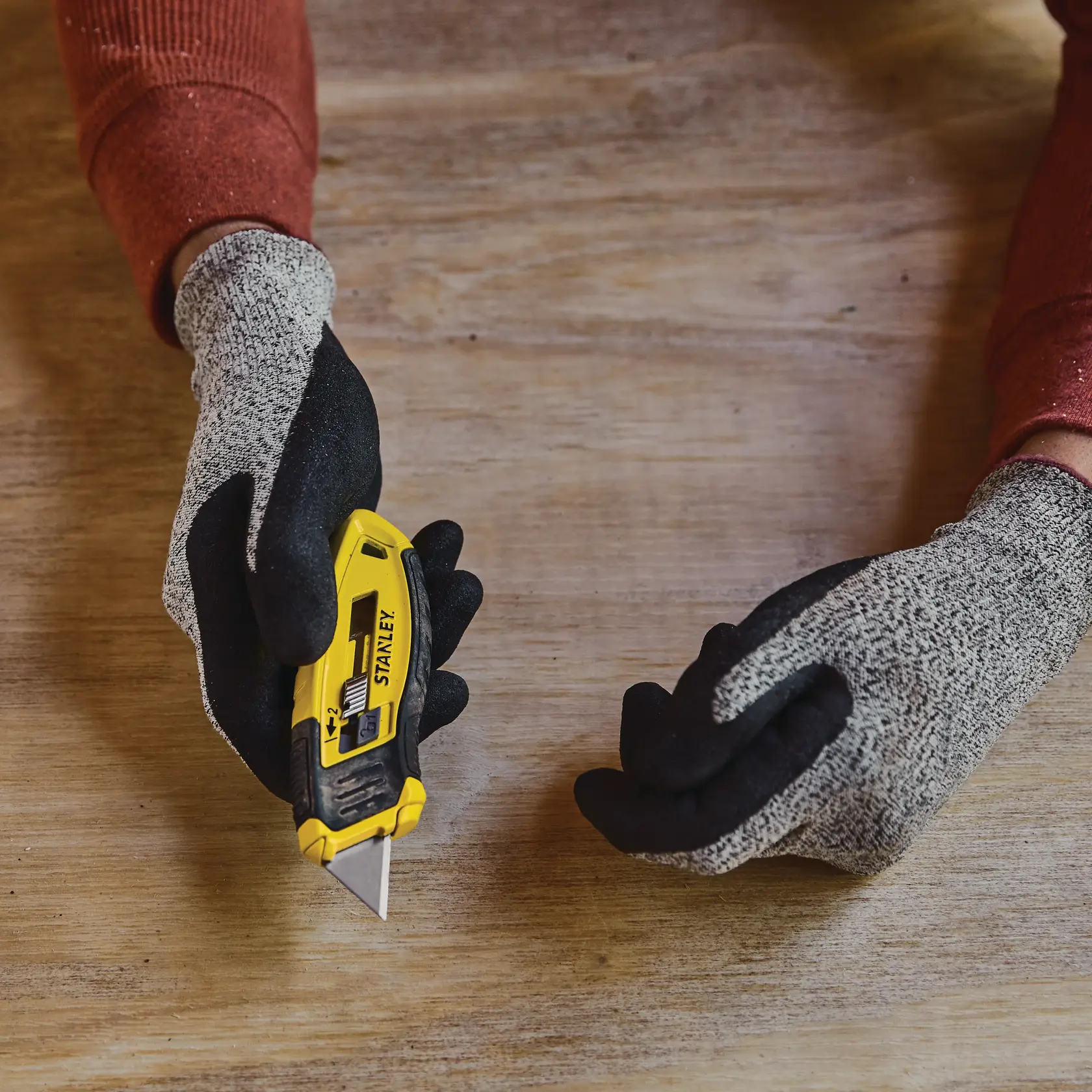 Foto des STANLEY STHT10432-0 Cuttermesser in behandschuhter Hand auf Holztisch.