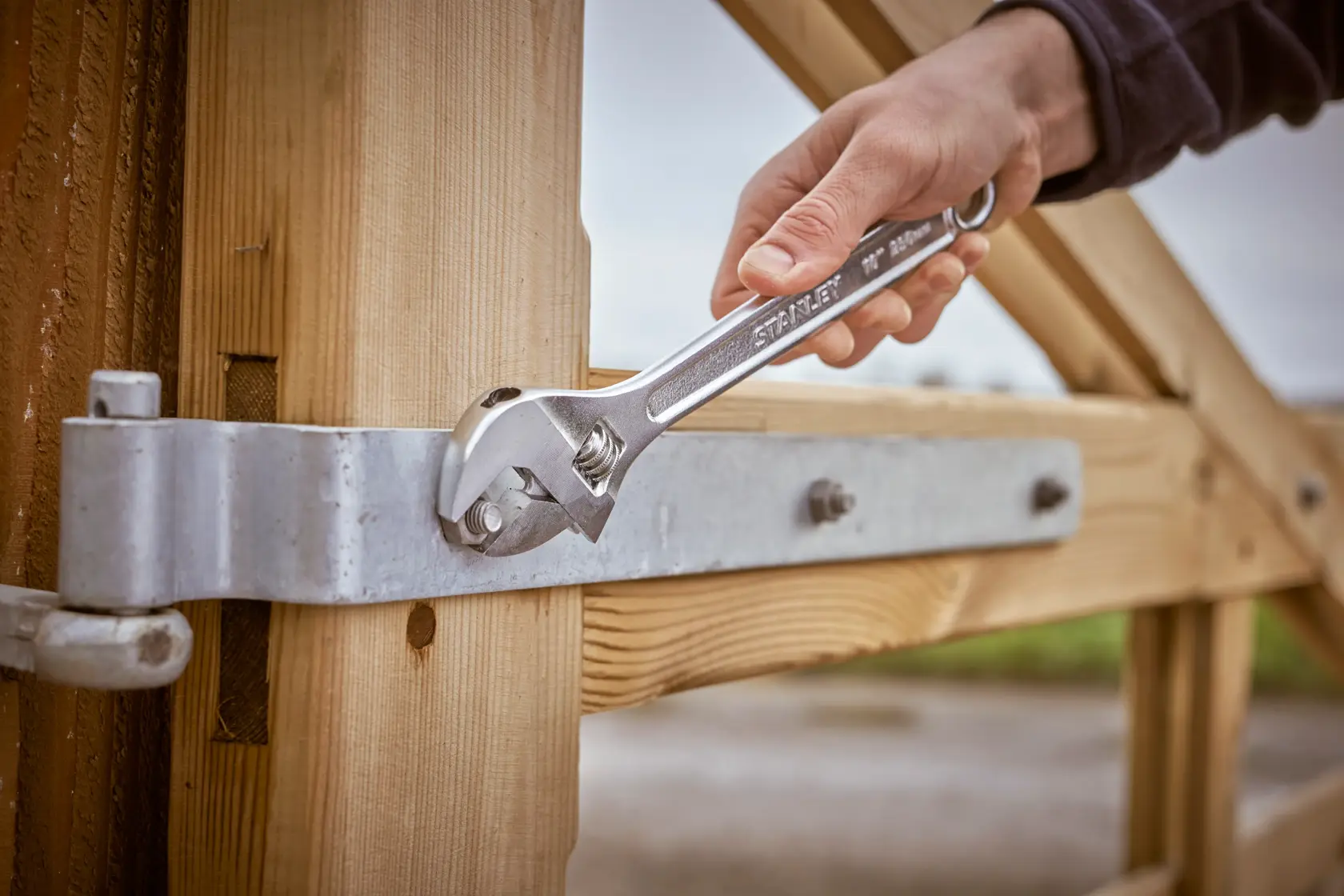 STANLEY STHT13156-0 adjustable wrench tightening metal bolt on wooden gate, close-up outdoor photography.