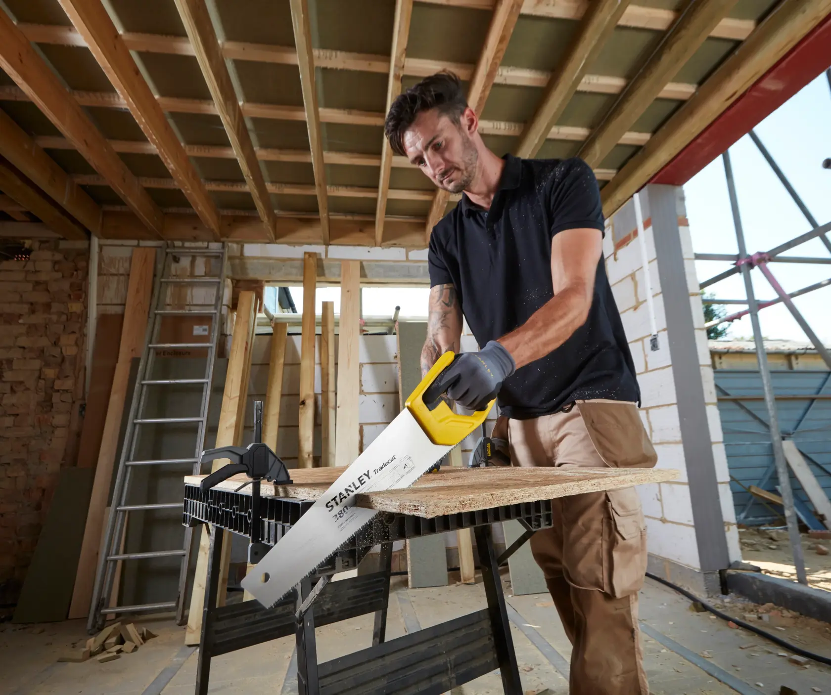 STANLEY STHT20348-1 Handsäge mit gelbem Griff schneidet Holzplatte auf Baustelle.