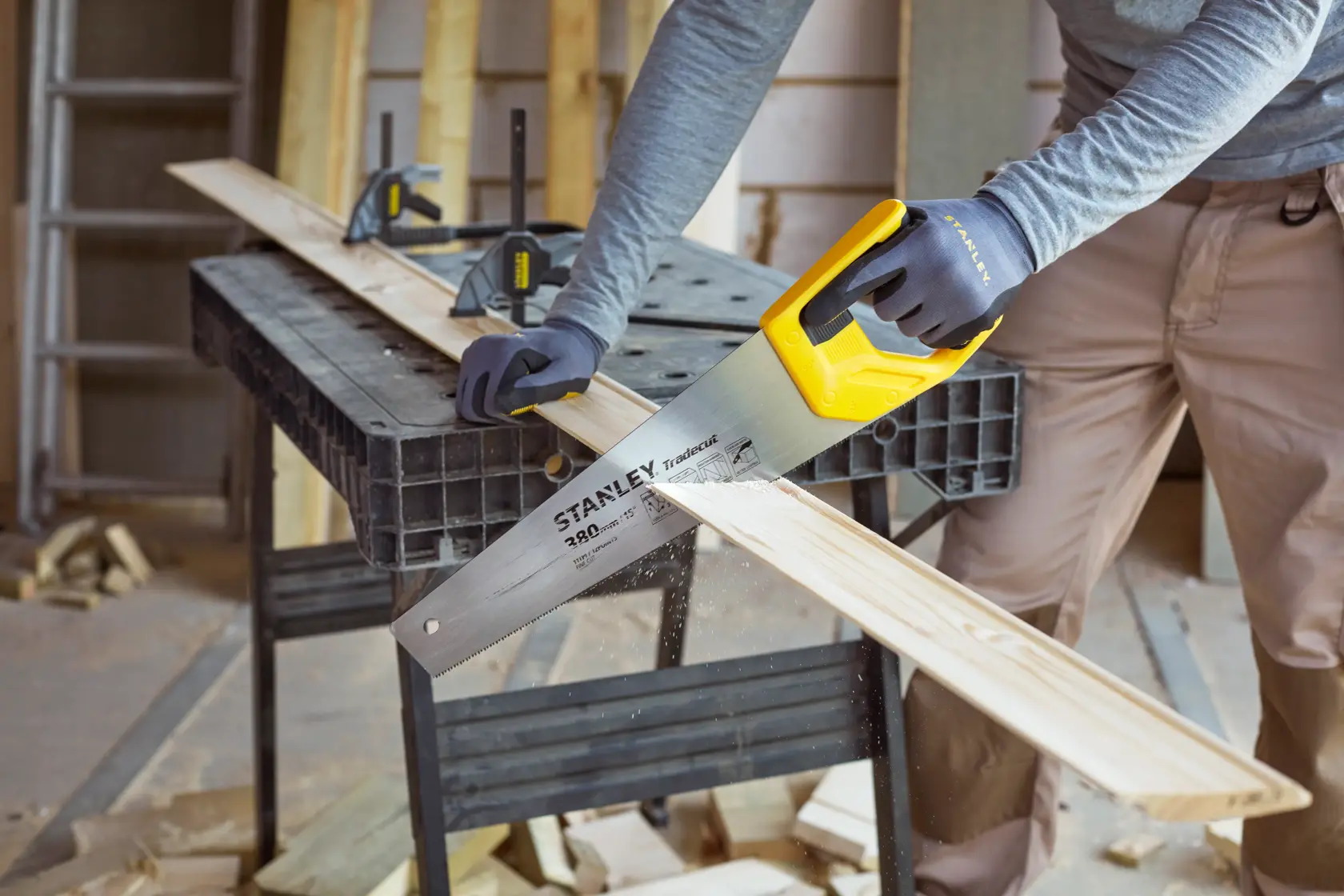 Stanley STHT20349-1 Handsäge mit gelbem Griff schneidet ein Holzbrett auf Werkbank, Nahaufnahme.