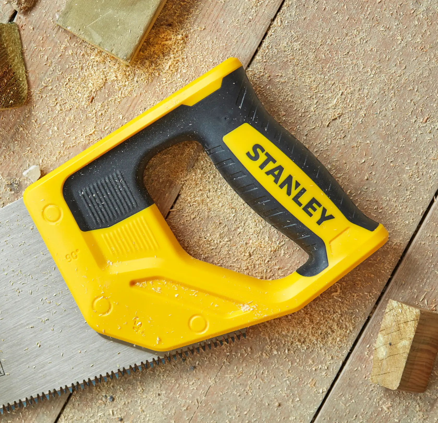 STANLEY STHT20349-1 Handsäge mit gelbem und schwarzem Griff, Nahaufnahme auf Holzoberfläche mit Sägespänen.