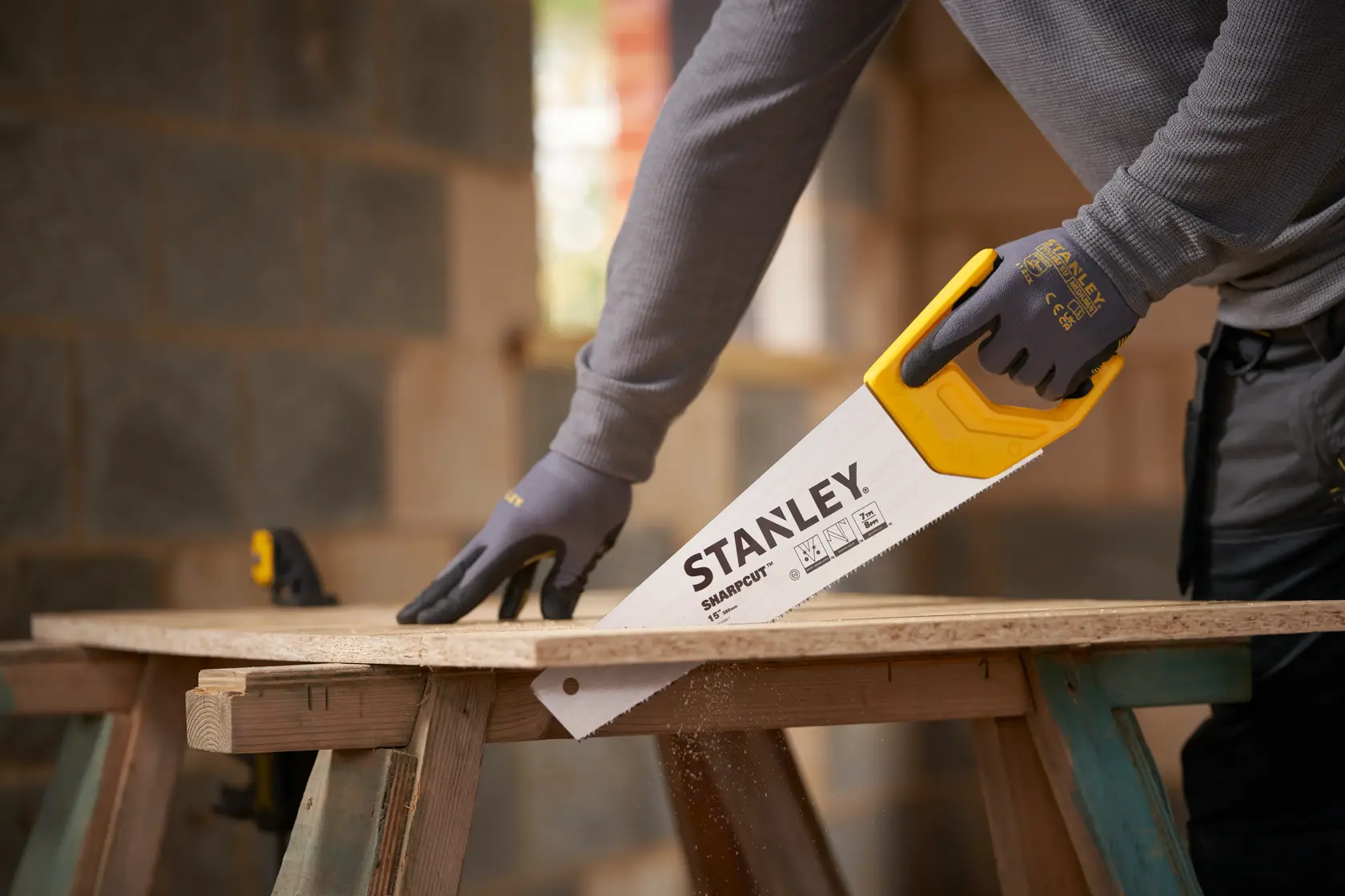 Foto der STANLEY STHT20366-1 Handsäge mit gelbem Griff beim Sägen von Holz, verwendet von einer Person mit Handschuhen.
