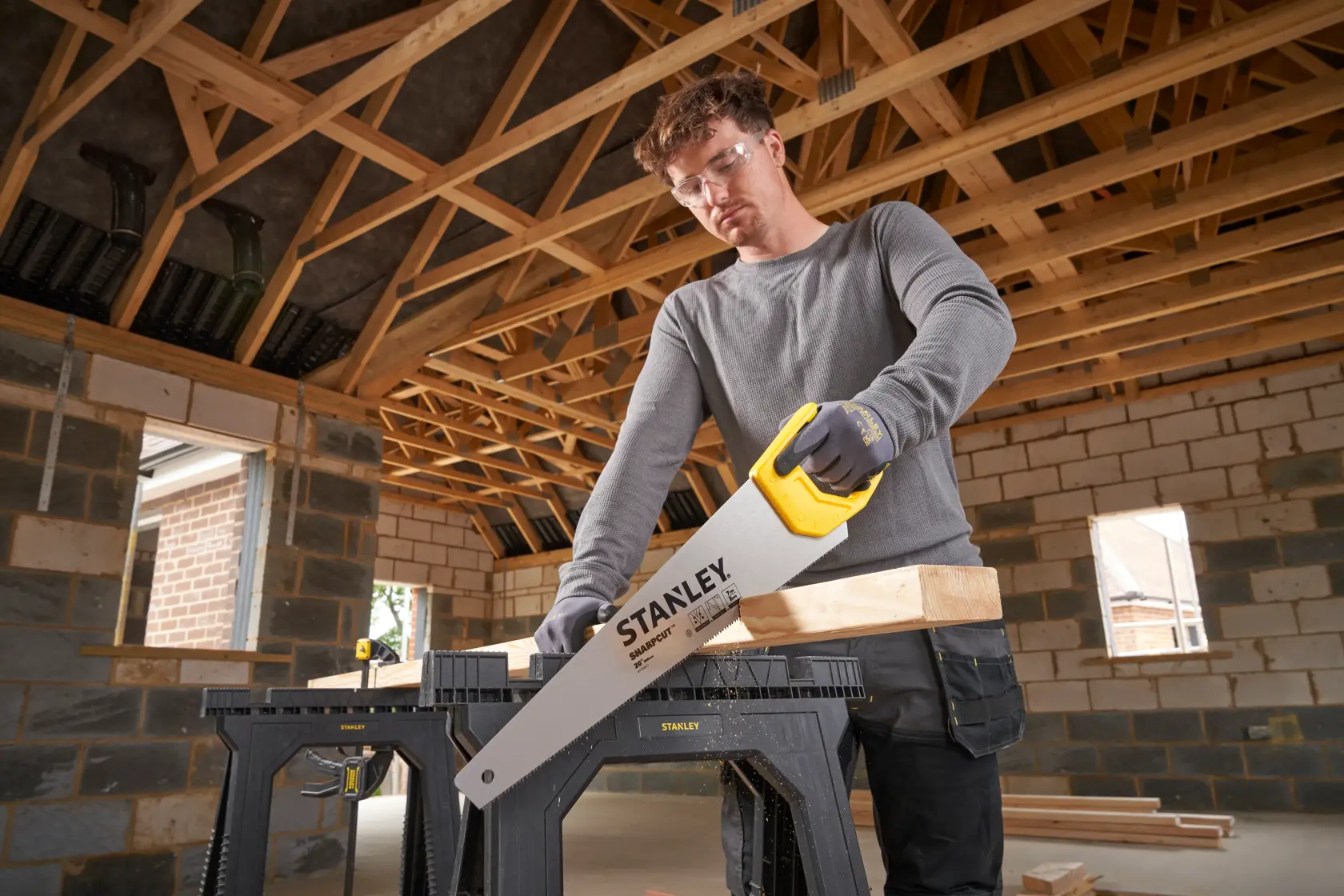 Foto der STANLEY STHT20367-1 Handsäge mit gelbem Griff, sägt Holz auf einer Sägebock in einem Rohbau.