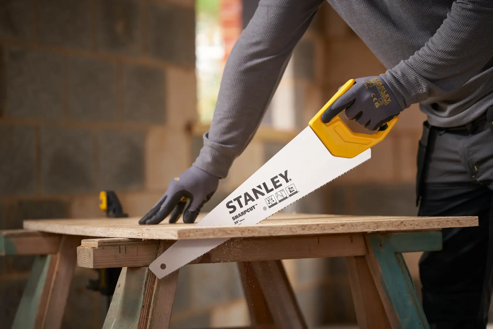 STANLEY STHT20367-1 Handsäge mit gelbem Griff schneidet Holz, Seitenansicht, verwendet von Person mit Handschuhen.