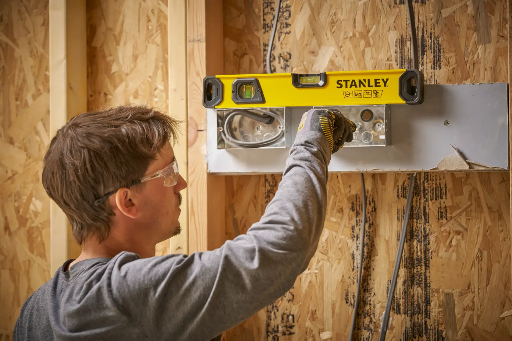 Eine Person verwendet eine STANLEY Wasserwaage (Modell STHT41016-0), um die Ausrichtung eines Metallteils an einer im Bau befindlichen Holzwand zu überprüfen.