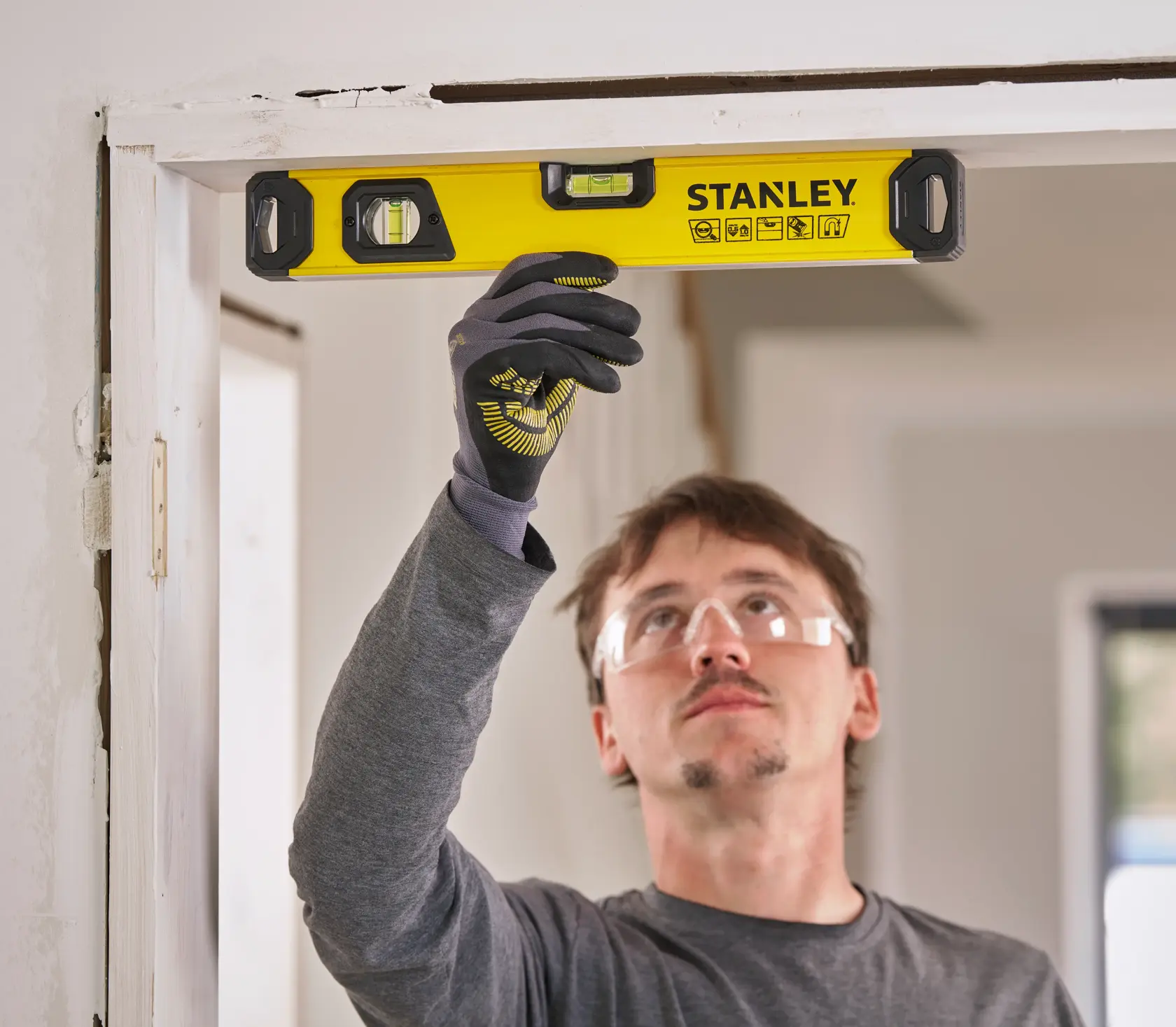 Eine Person mit Arbeitshandschuhen verwendet eine gelbe STANLEY Wasserwaage, um die Ausrichtung eines Türrahmens zu überprüfen.