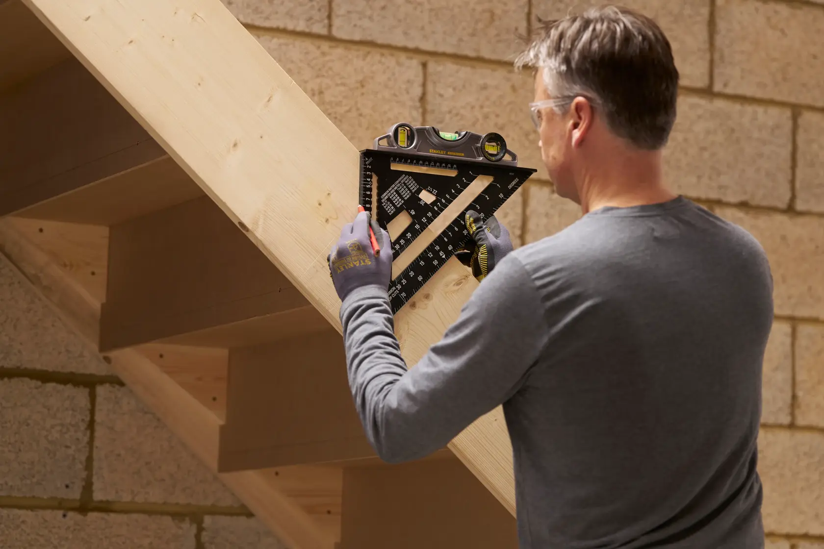 STANLEY STHT46102-0 carpenter using black layout square with level on wooden stairs.