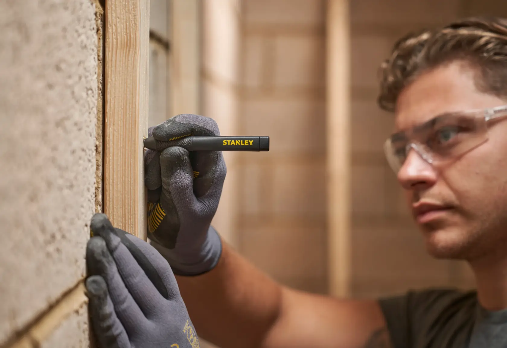 Person mit Handschuhen nutzt einen STANLEY Markierstift, um Linien auf Holz während Bauarbeiten zu ziehen.
