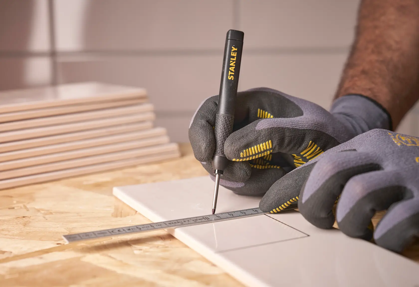 Behandschuhte Hände markieren mit einem STANLEY Werkzeug und Lineal Linien auf einer Fliese.