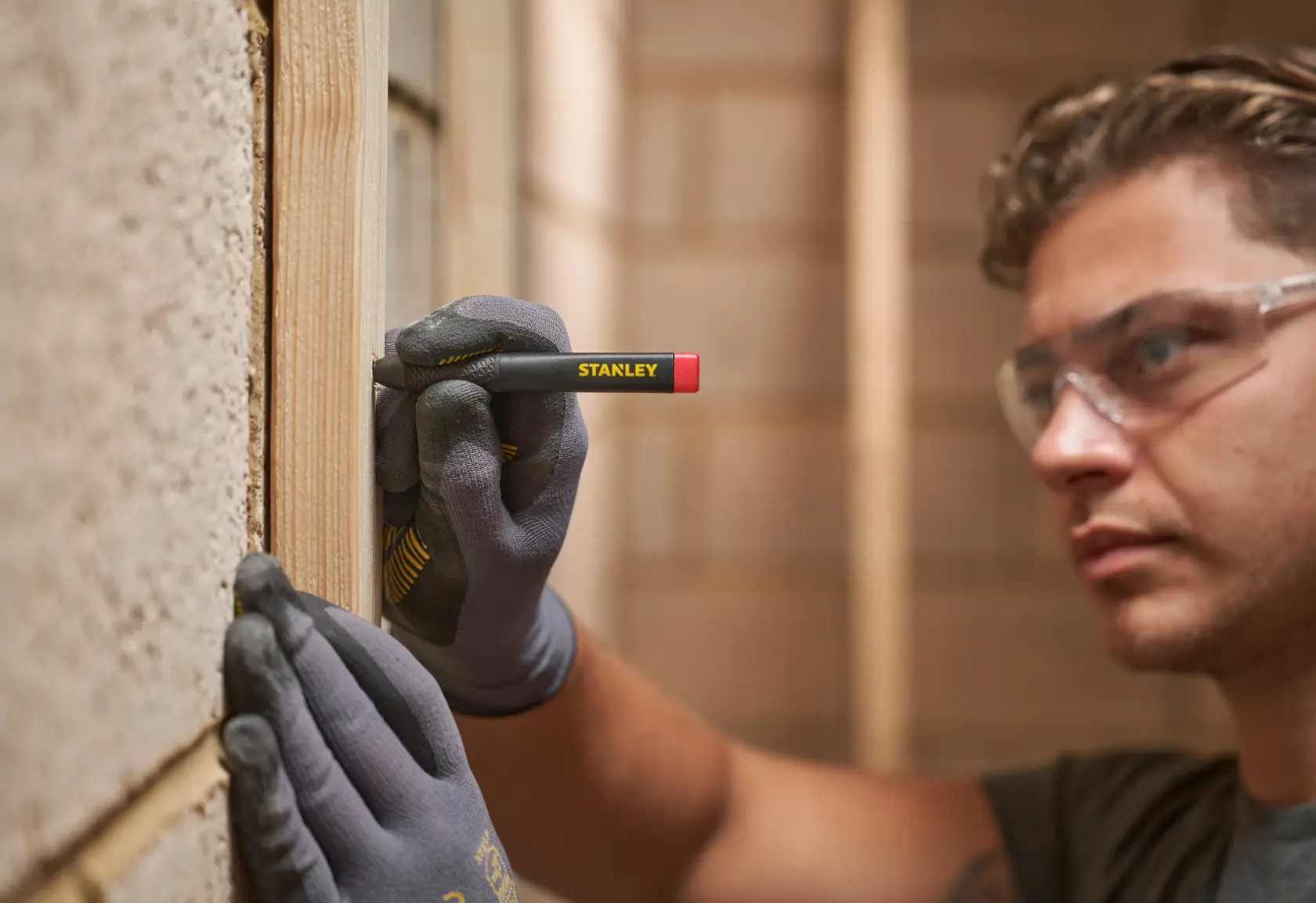 Person markiert Holz mit einem STANLEY Zimmermannsbleistift, trägt Handschuhe und Schutzbrille.