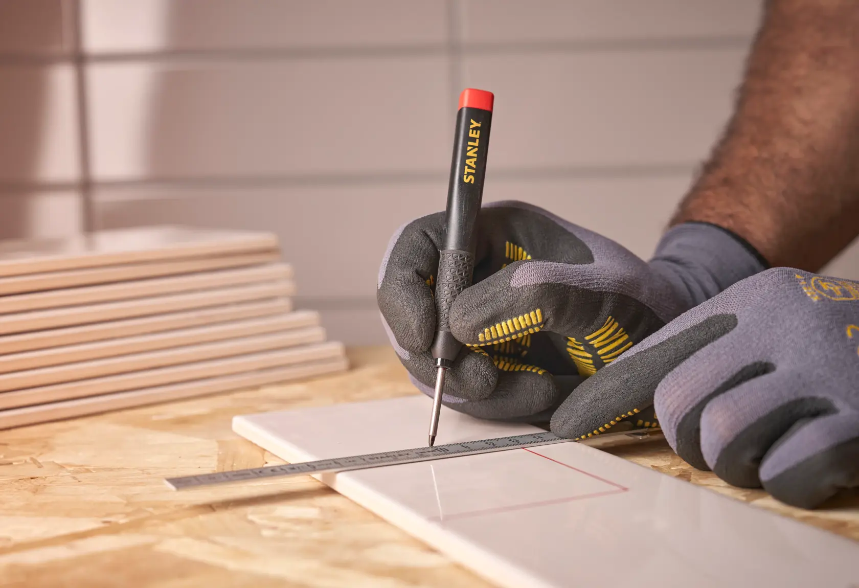 Behandschuhte Hände markieren eine Fliese mit STANLEY Werkzeug und Metalllineal.