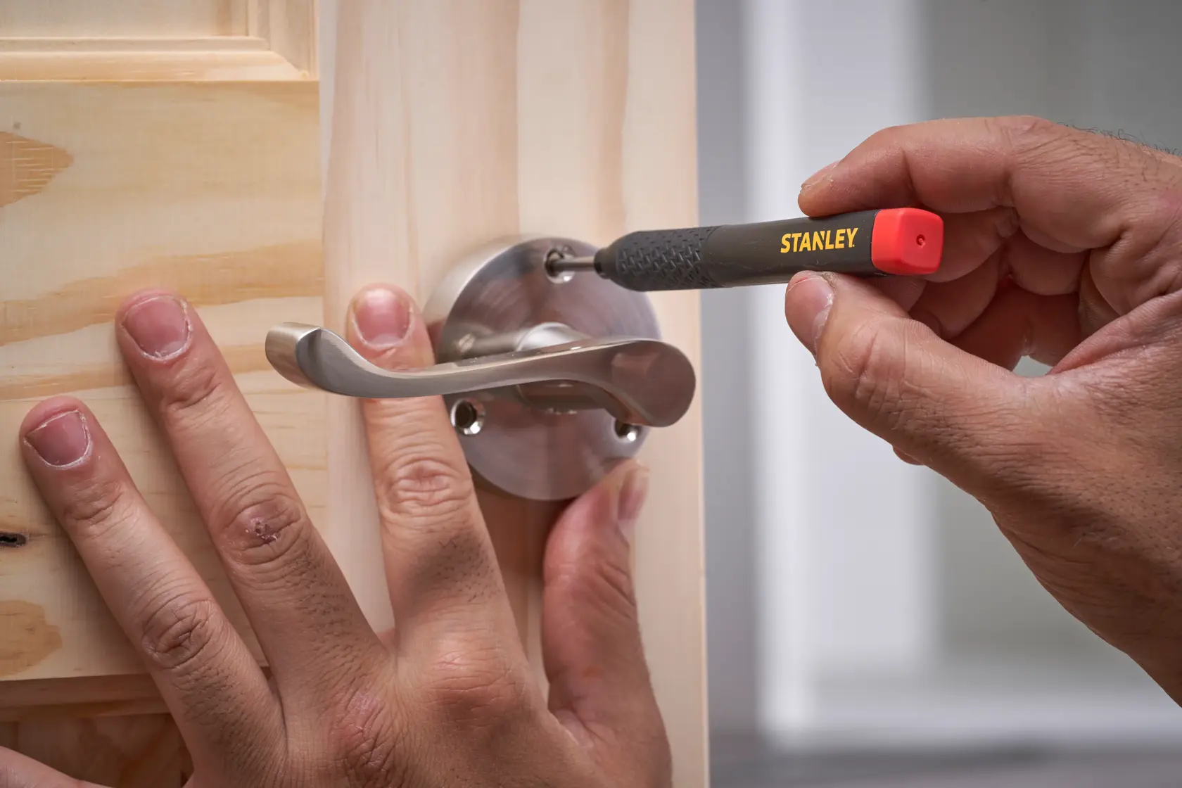 Mit einem STANLEY Werkzeug wird eine Schraube am Metall-Türgriff auf einer Holztür festgezogen.