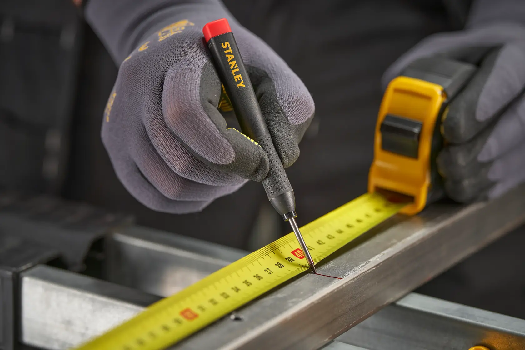 Behandschuhte Hände markieren mit Stanley Werkzeug und Maßband Maße auf einer Metallfläche.