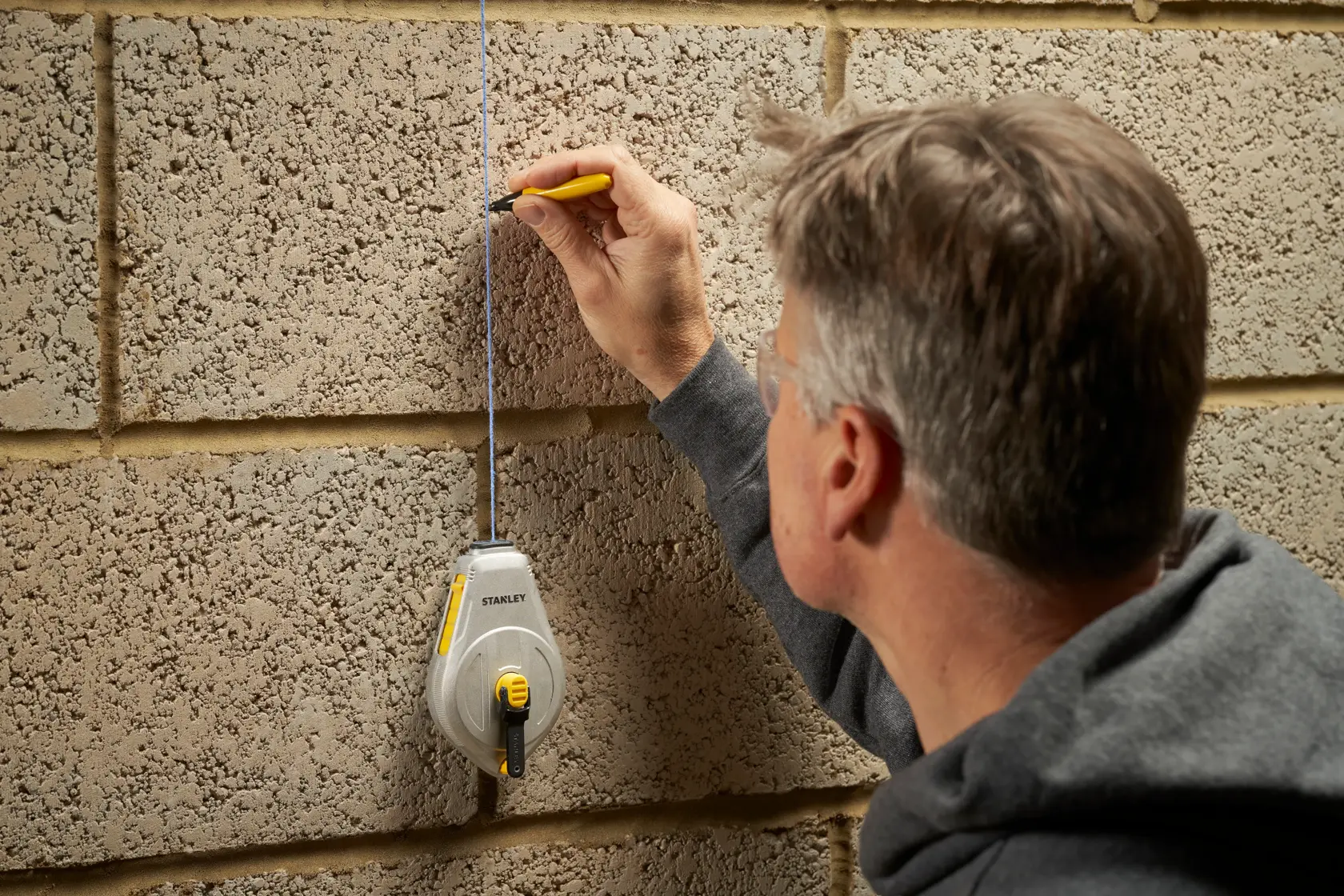 STANLEY STHT47110-0 chalk line reel used on a concrete wall with person marking a straight line.