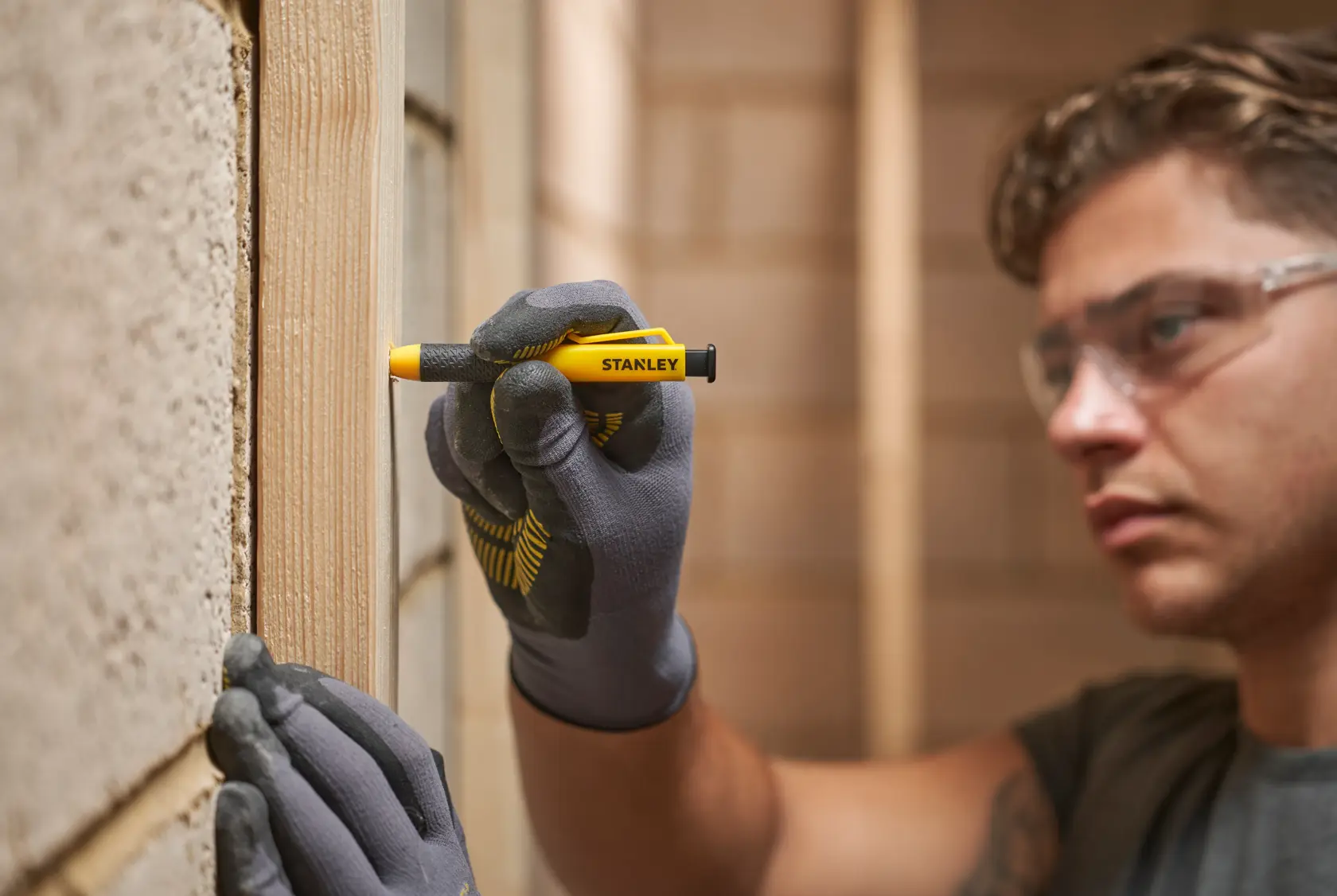 Person mit Handschuhen markiert einen Holzträger drinnen mit einem Stanley Zimmermannsbleistift.