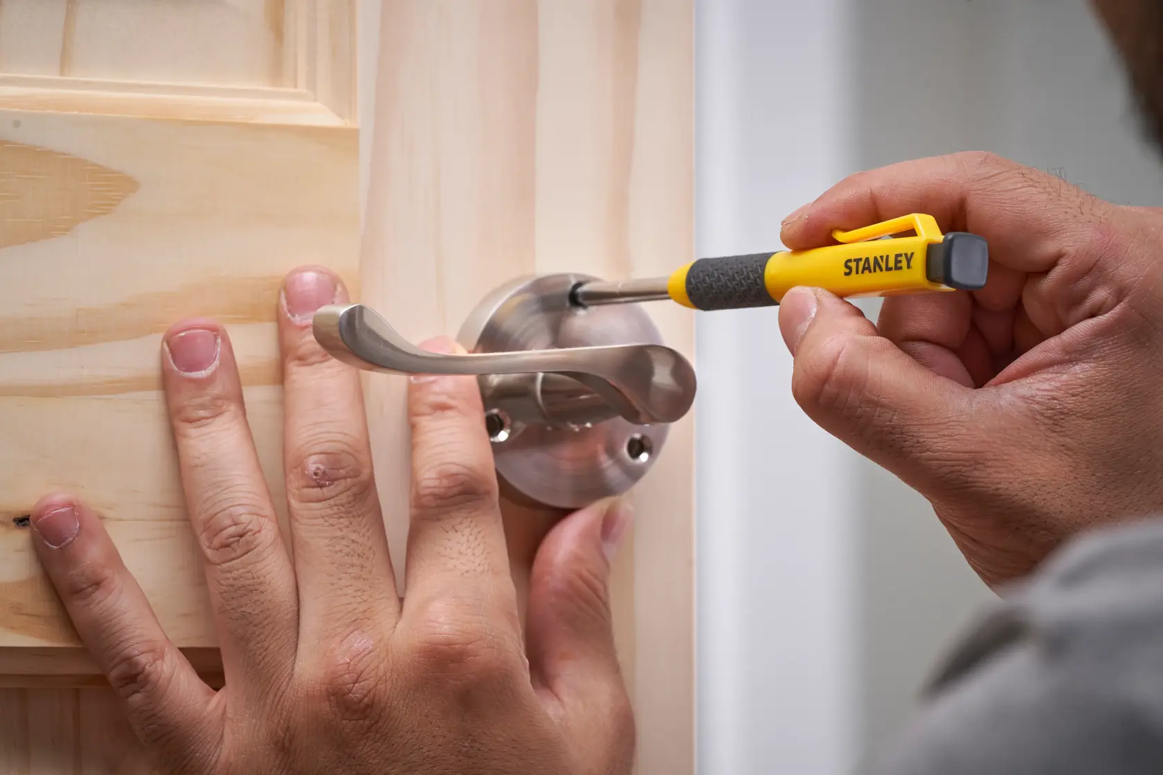Mit einem Stanley-Schraubendreher wird eine Schraube an einem Metall-Türgriff am Holztür befestigt.