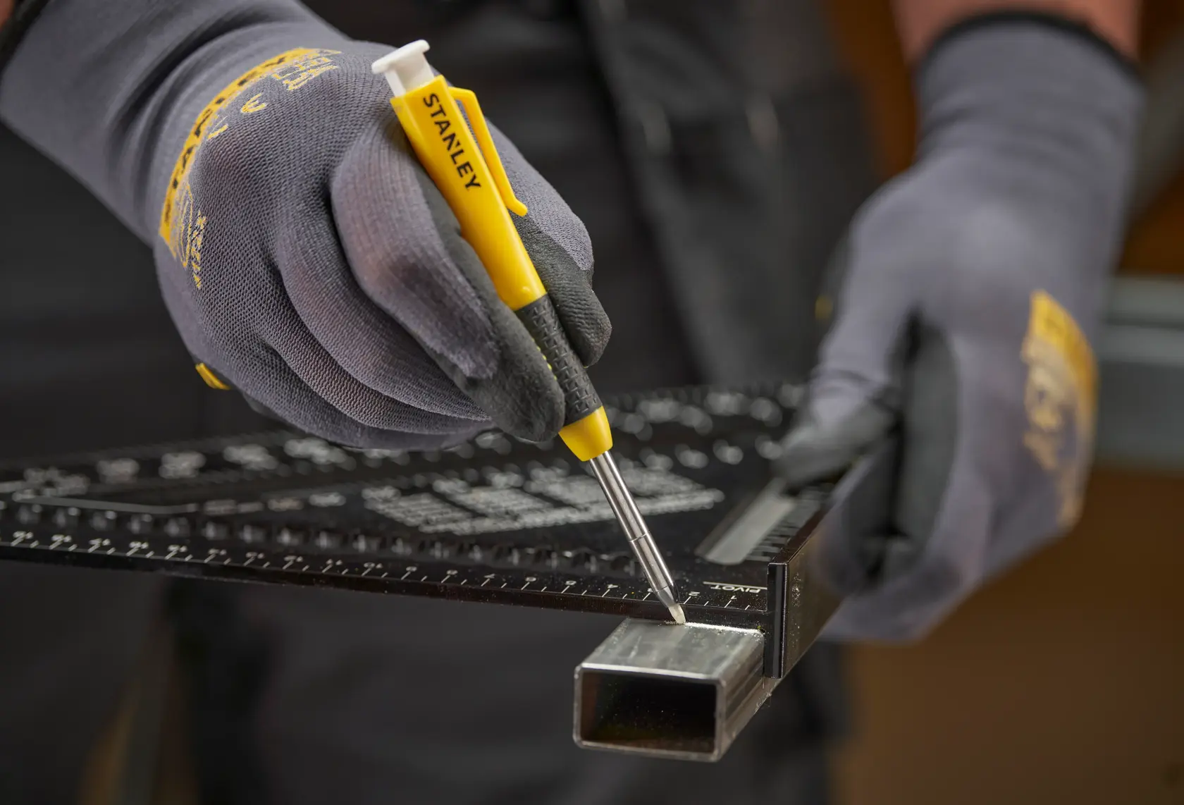 Behandschuhte Hände markieren ein Metallrohr mit STANLEY Markierwerkzeug und Lineal.
