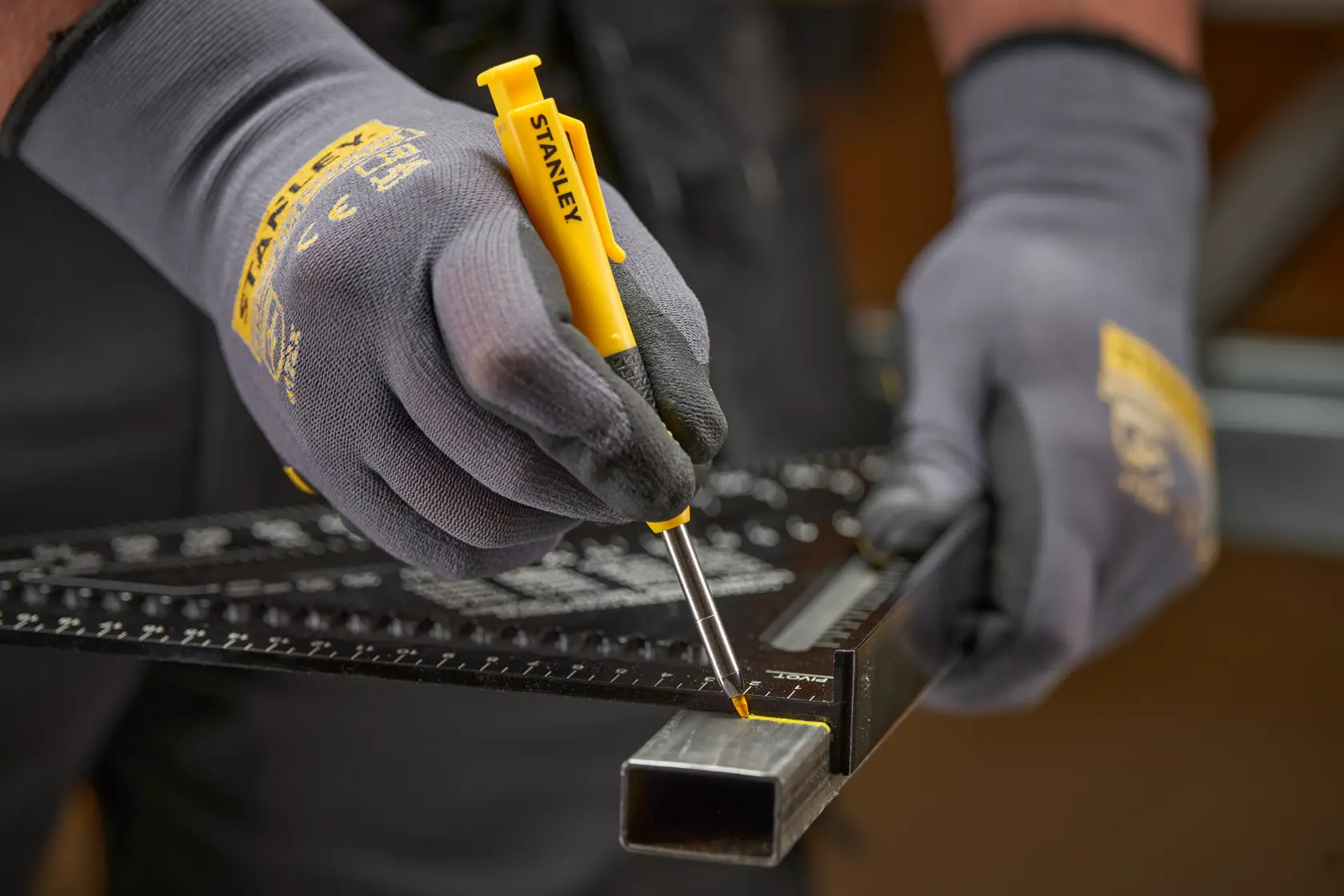 Behandschuhte Hände nutzen gelbes STANLEY Markierwerkzeug und Lineal an einem Metallrohr zum Messen.