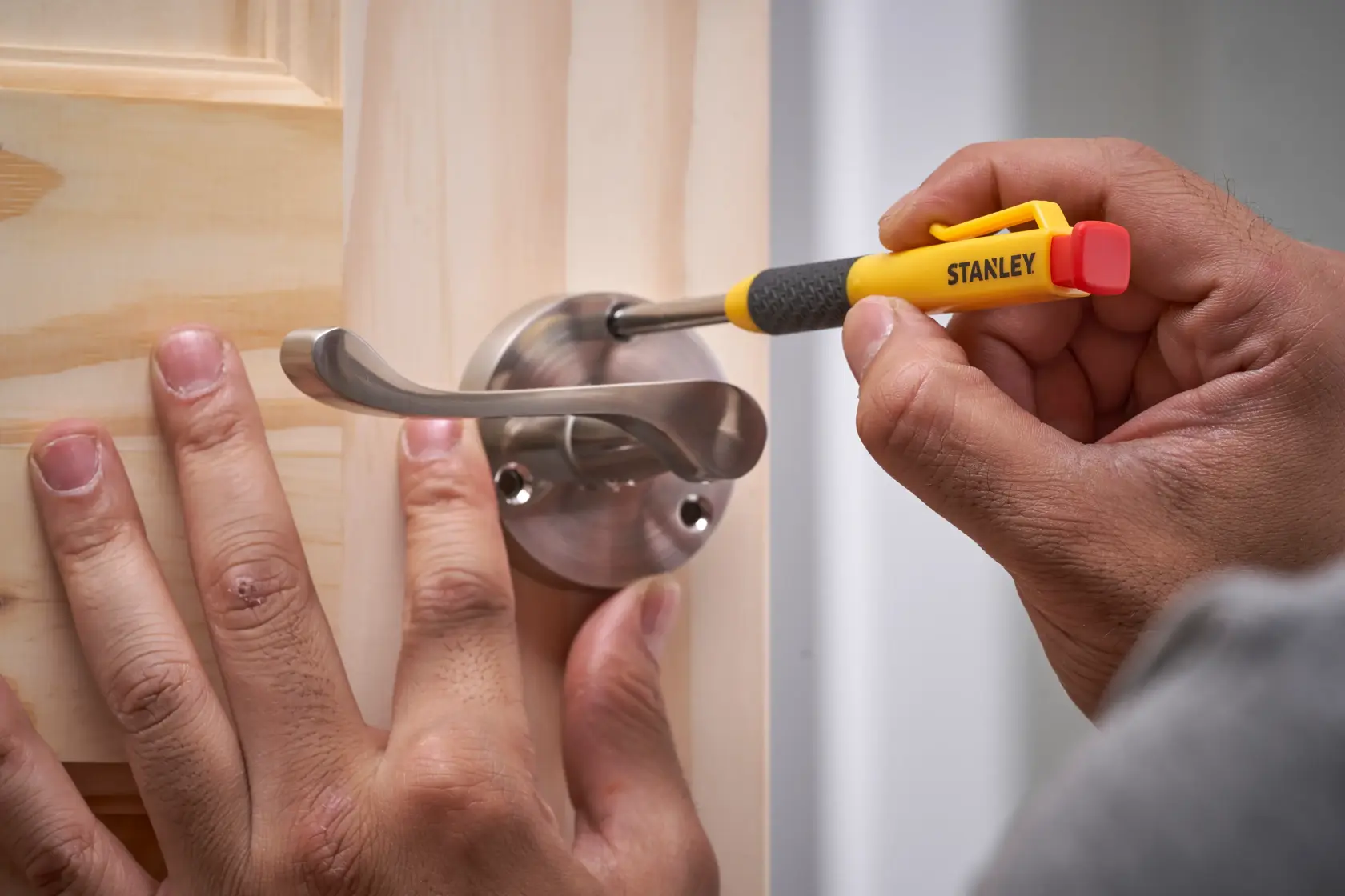 Person befestigt mit einem Stanley-Schraubendreher einen Metallgriff an einer Holztür.