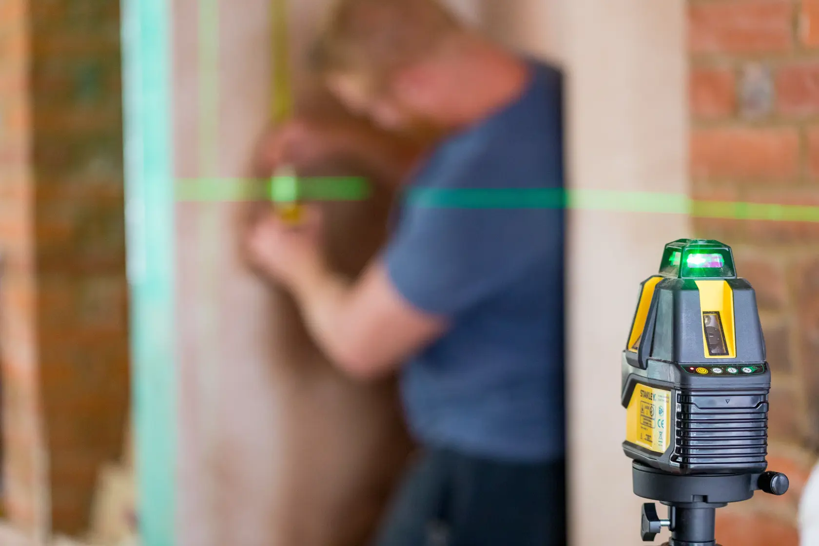 STANLEY STHT77524-1 Laser-Nivelliergerät projiziert grüne Linie auf Baustelle, Nahaufnahme seitlich.