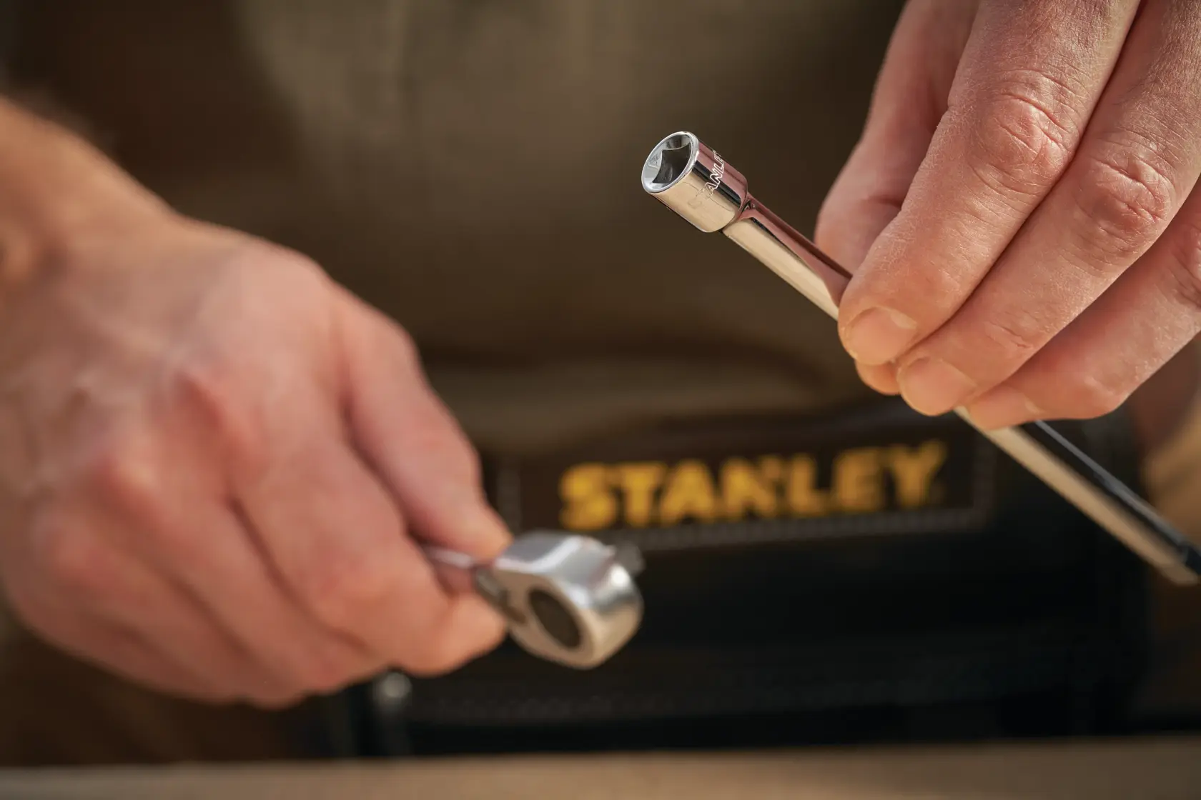 Foto des STANLEY STMT86007-0 Ratsche und Stecknuss, Nahaufnahme in der Hand, Werkzeugtasche sichtbar.