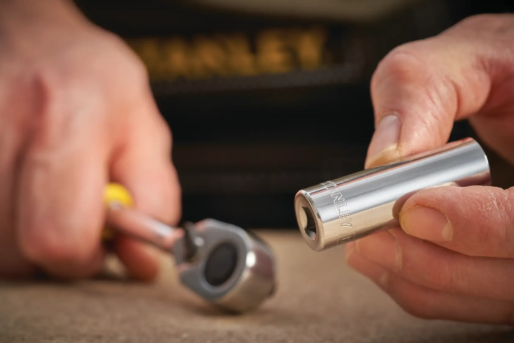 STANLEY STMT86097-0 Steckschlüssel in Hand mit Ratschen-Schlüssel auf Tisch, Nahaufnahme, Werkzeugfotografie.