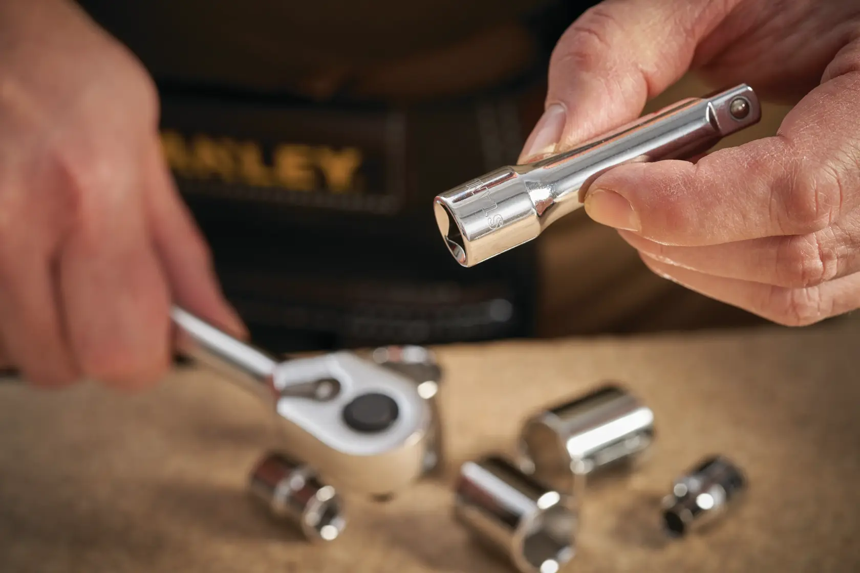 STANLEY STMT86206-0 Steckschlüssel-Verlängerung wird in der Hand gehalten, mit Ratsche und Stecknüssen auf der Werkbank.
