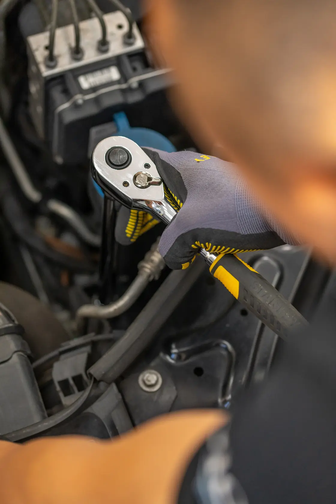 Foto des STANLEY STMT86207-0 Ratschenschlüssels im Einsatz am Automotor, Bediener mit Handschuhen.