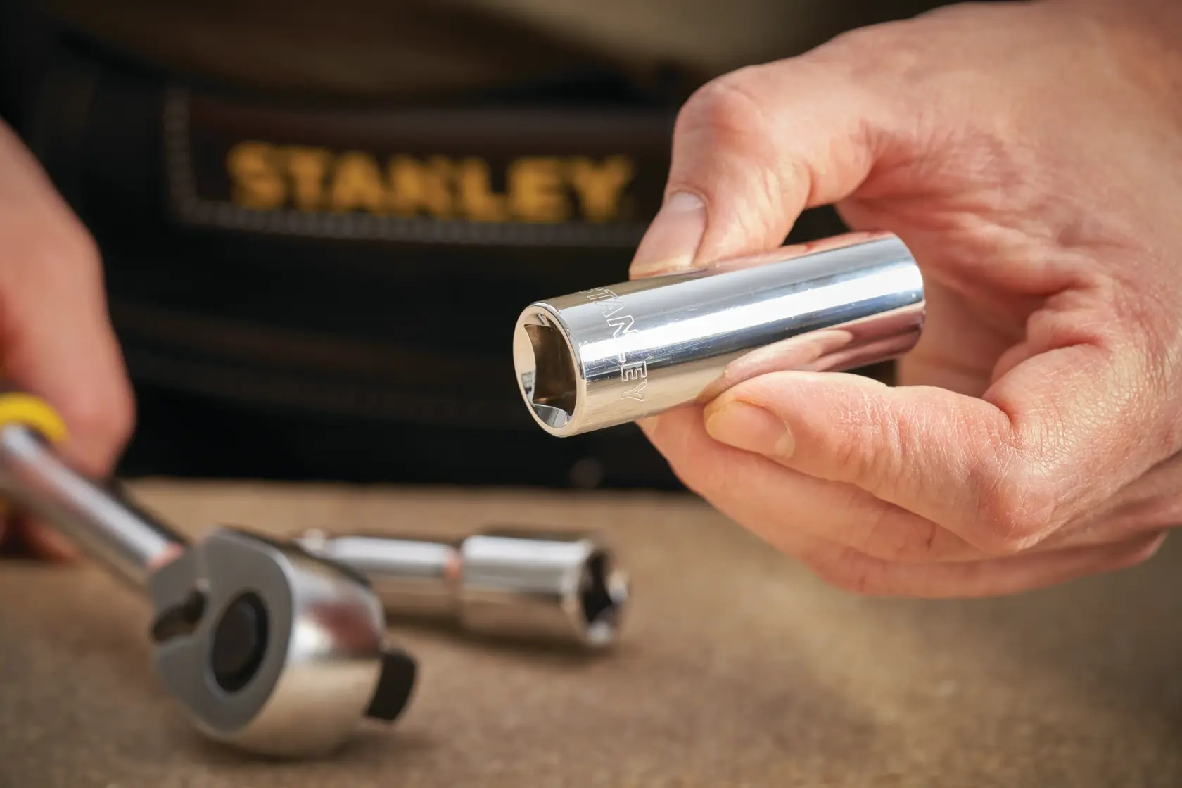 Foto des STANLEY STMT88994-0 Chrom-Steckschlüssels in der Hand, Ratsche und Verlängerung auf dem Tisch.