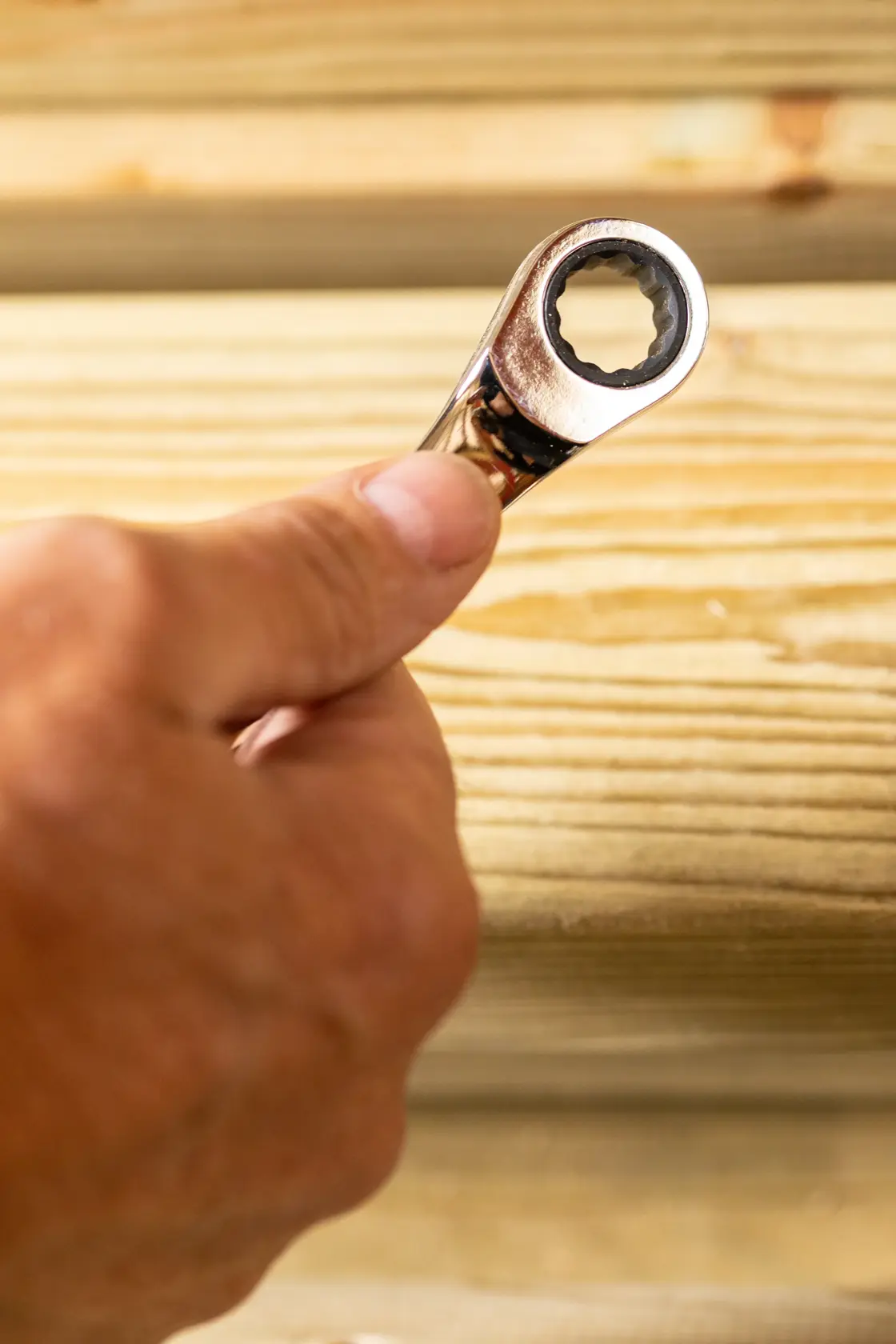 STANLEY STMT89909-0 ratcheting wrench held in hand against wooden boards, close-up photography.